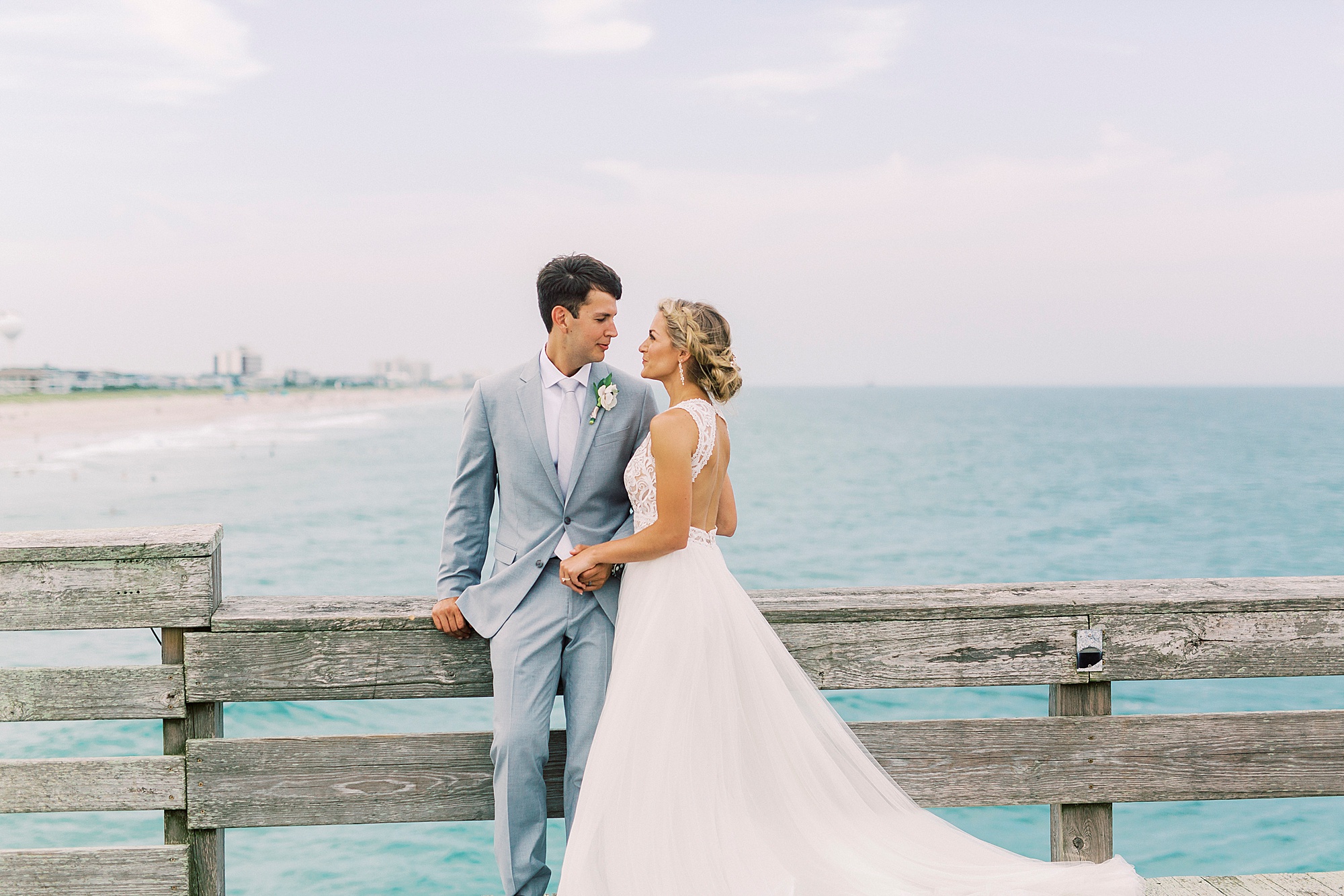 bride and groom stand on pier with ocean behind them at Wrightsville Beach