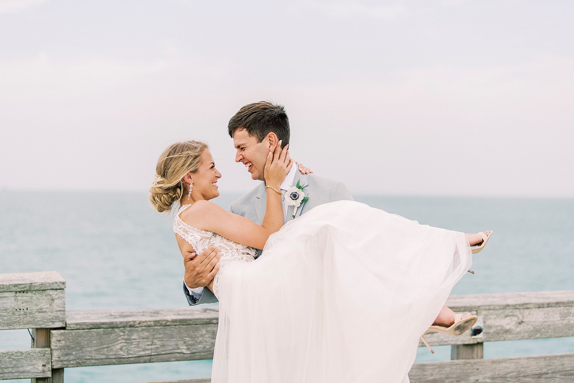 groom lifts bride up on pier at Wrightsville Beach