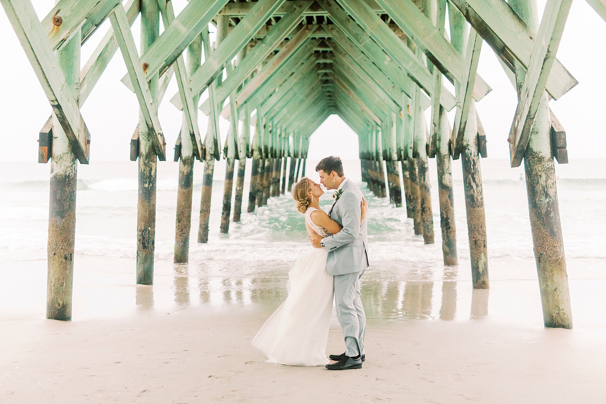 bride and groom hug under pier at Oceanic Restaurant