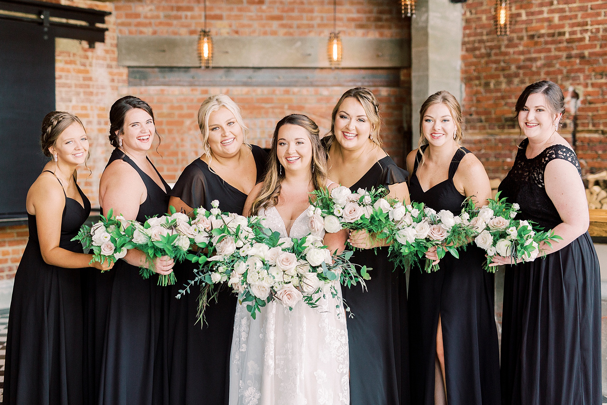 bride poses with bridesmaids in black gowns at the Cadillac Service Garage