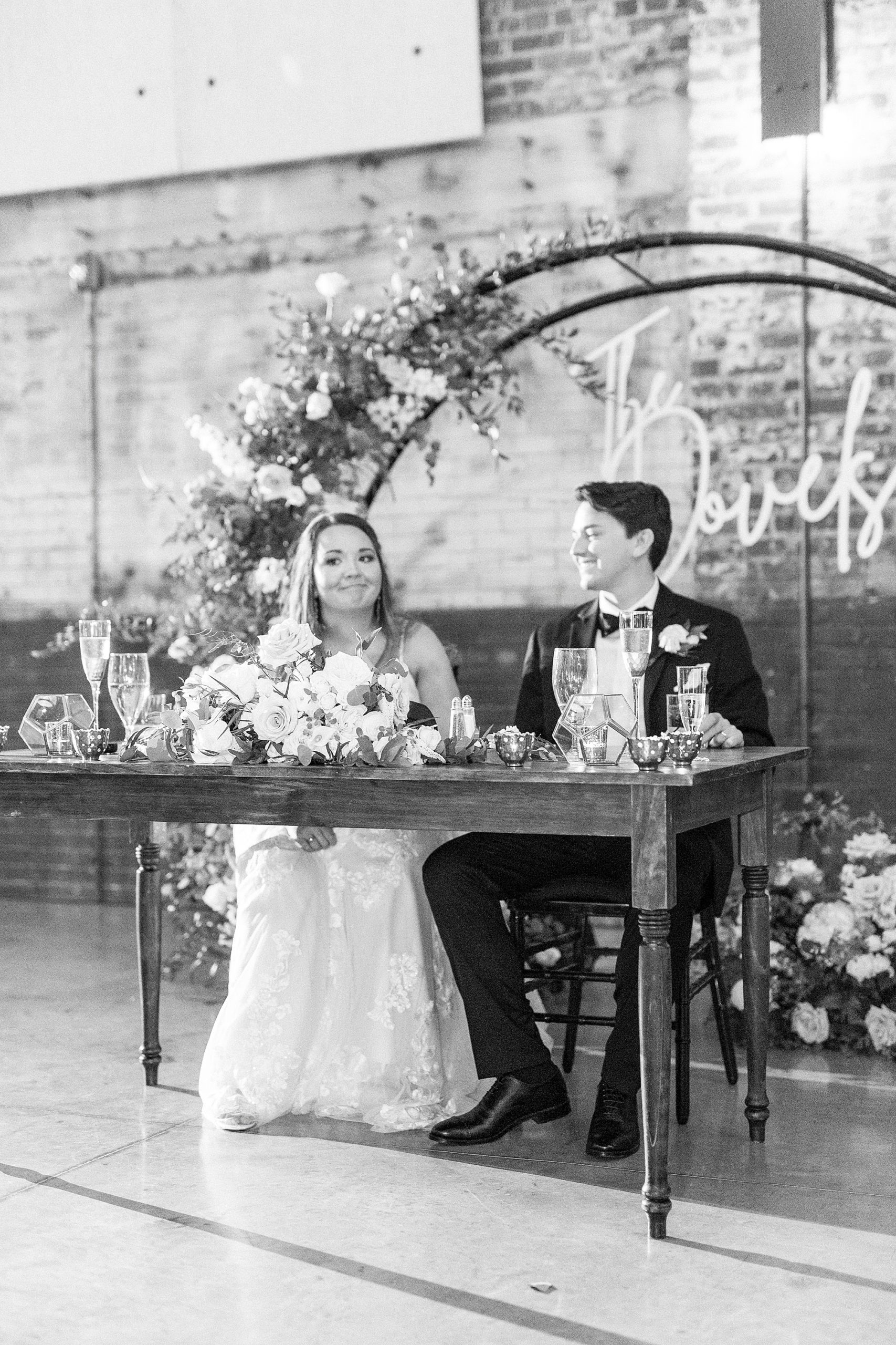 newlyweds sit at head table under neon sign