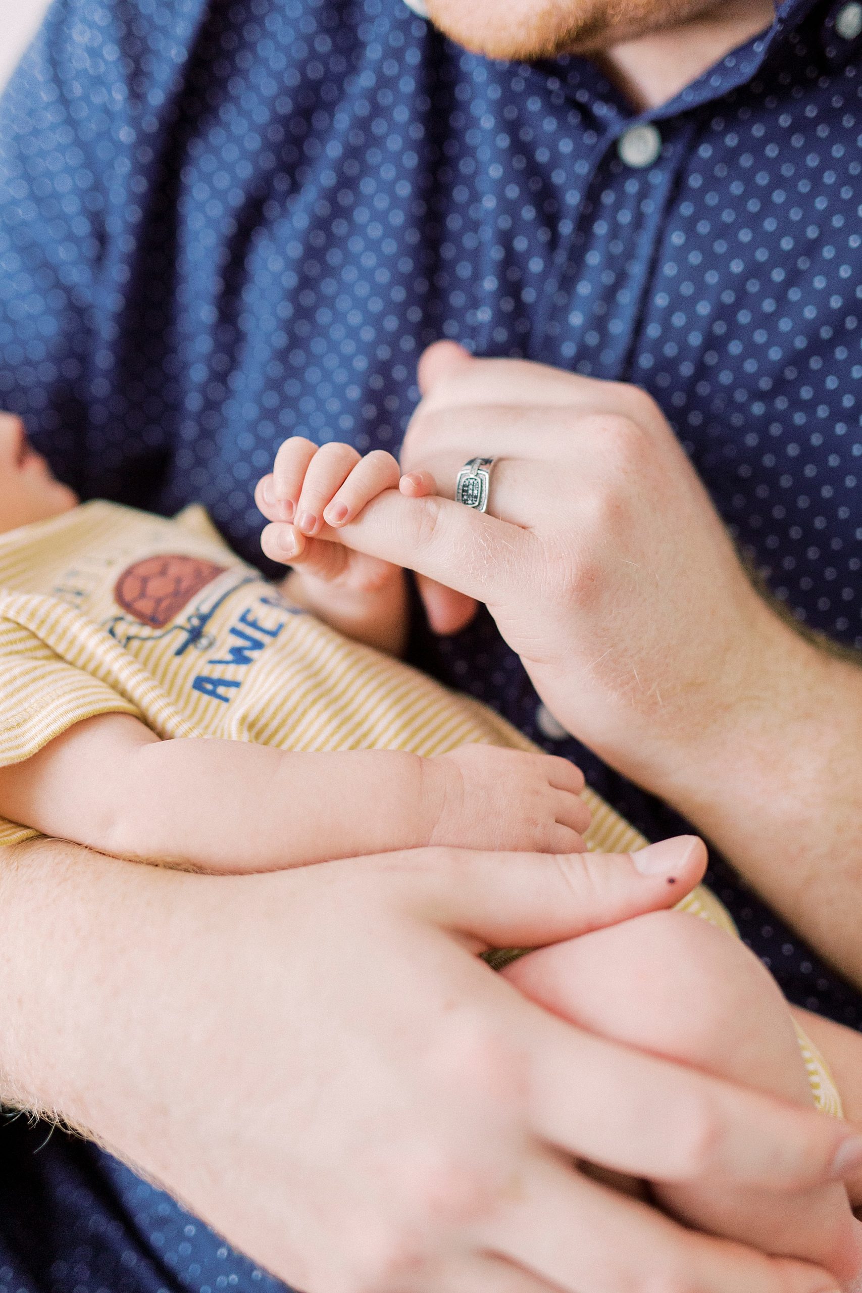 dad holds son's finger during newborn photos at home