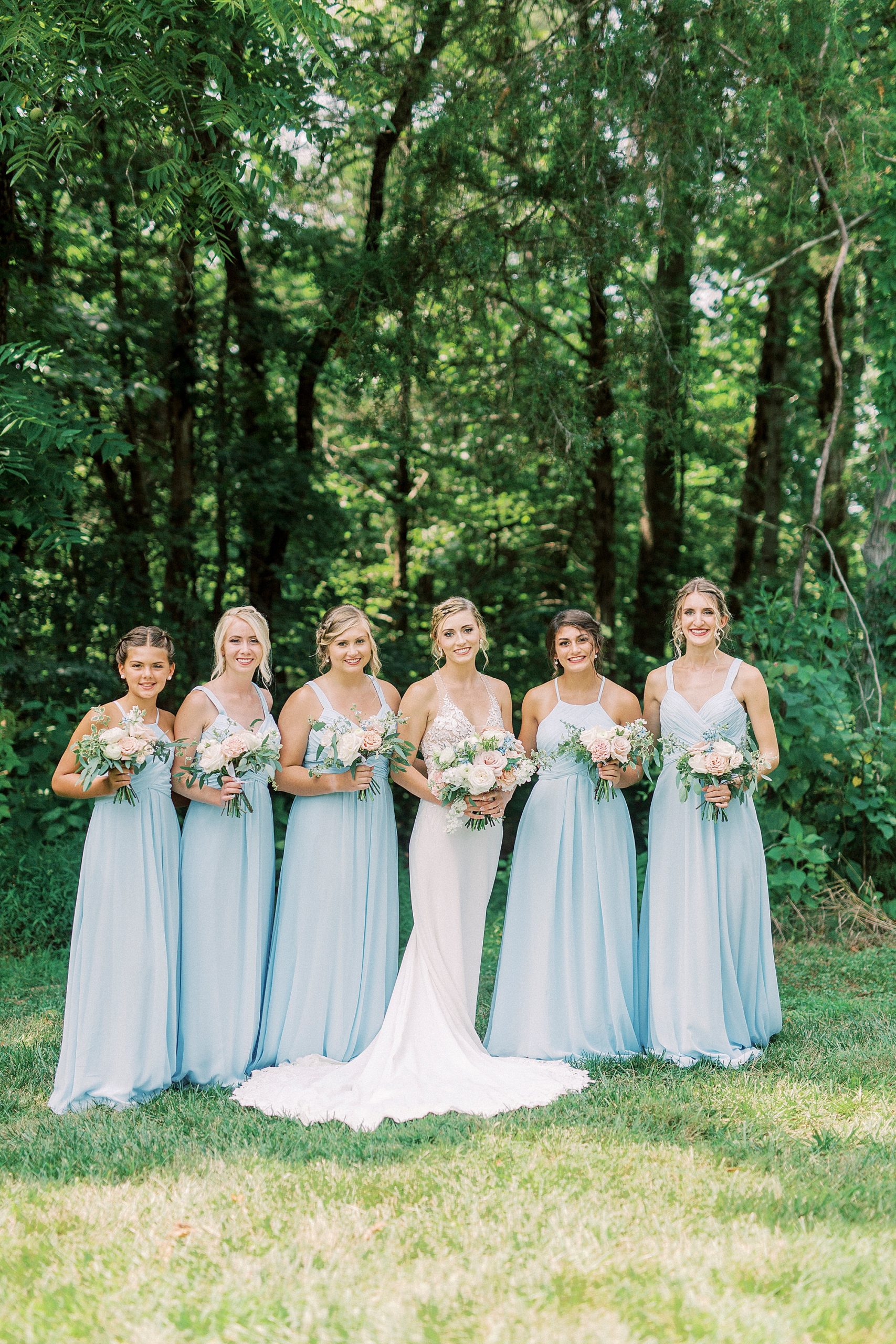 bride and bridesmaids in blue gowns pose before Winston Salem wedding