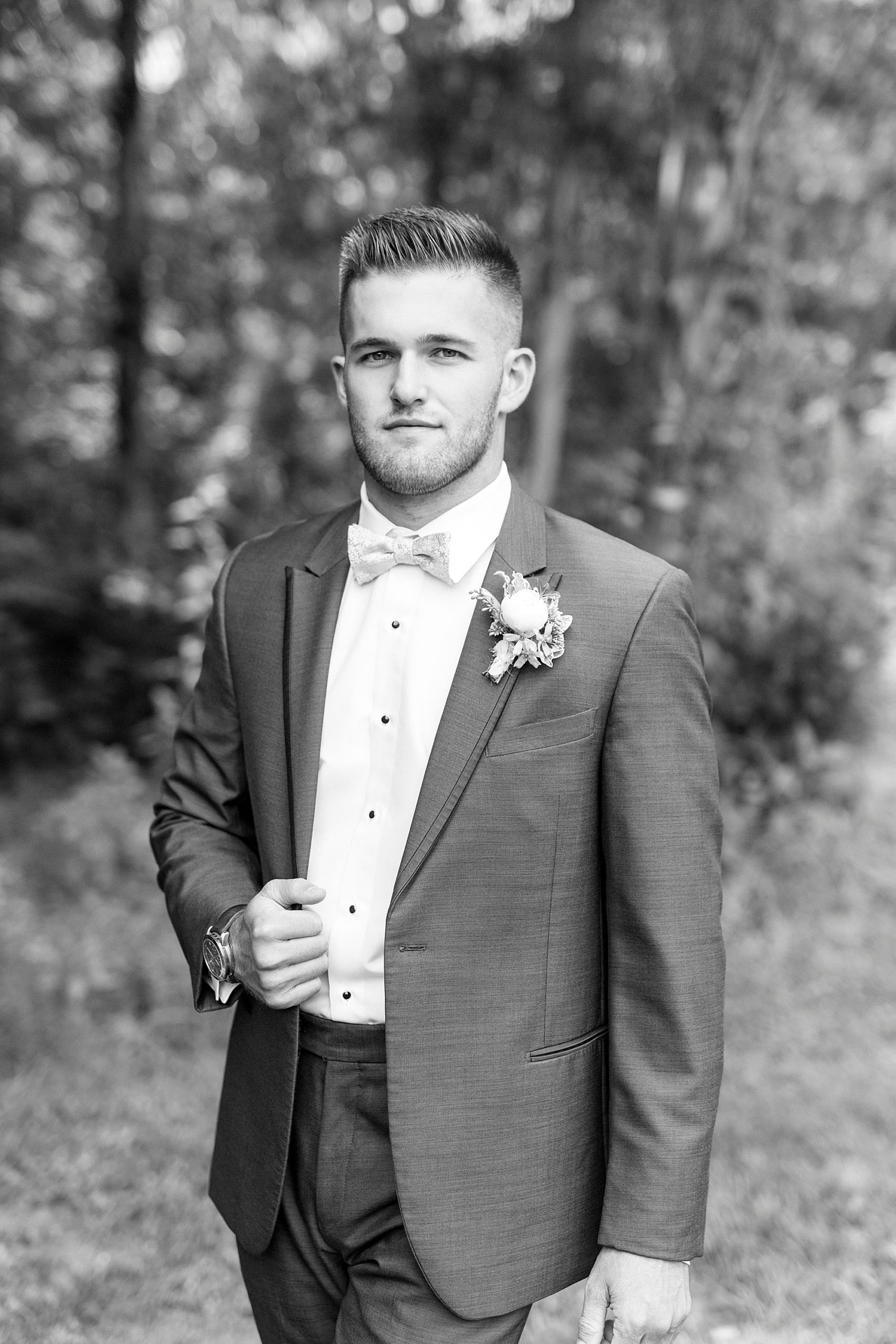 groom holds lapel of suit jacket