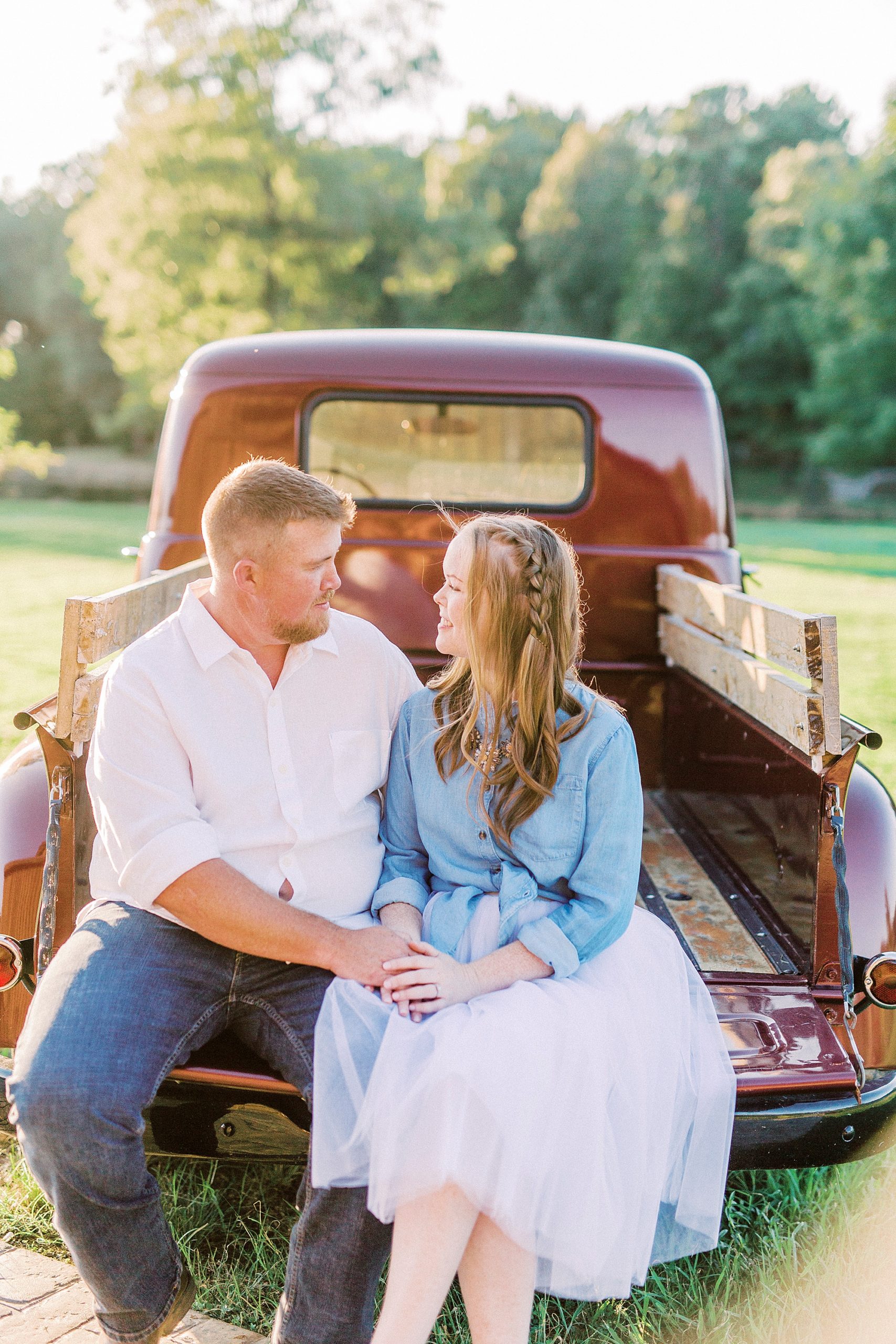 engaged couple sits on tcuk bed of vintage red truck