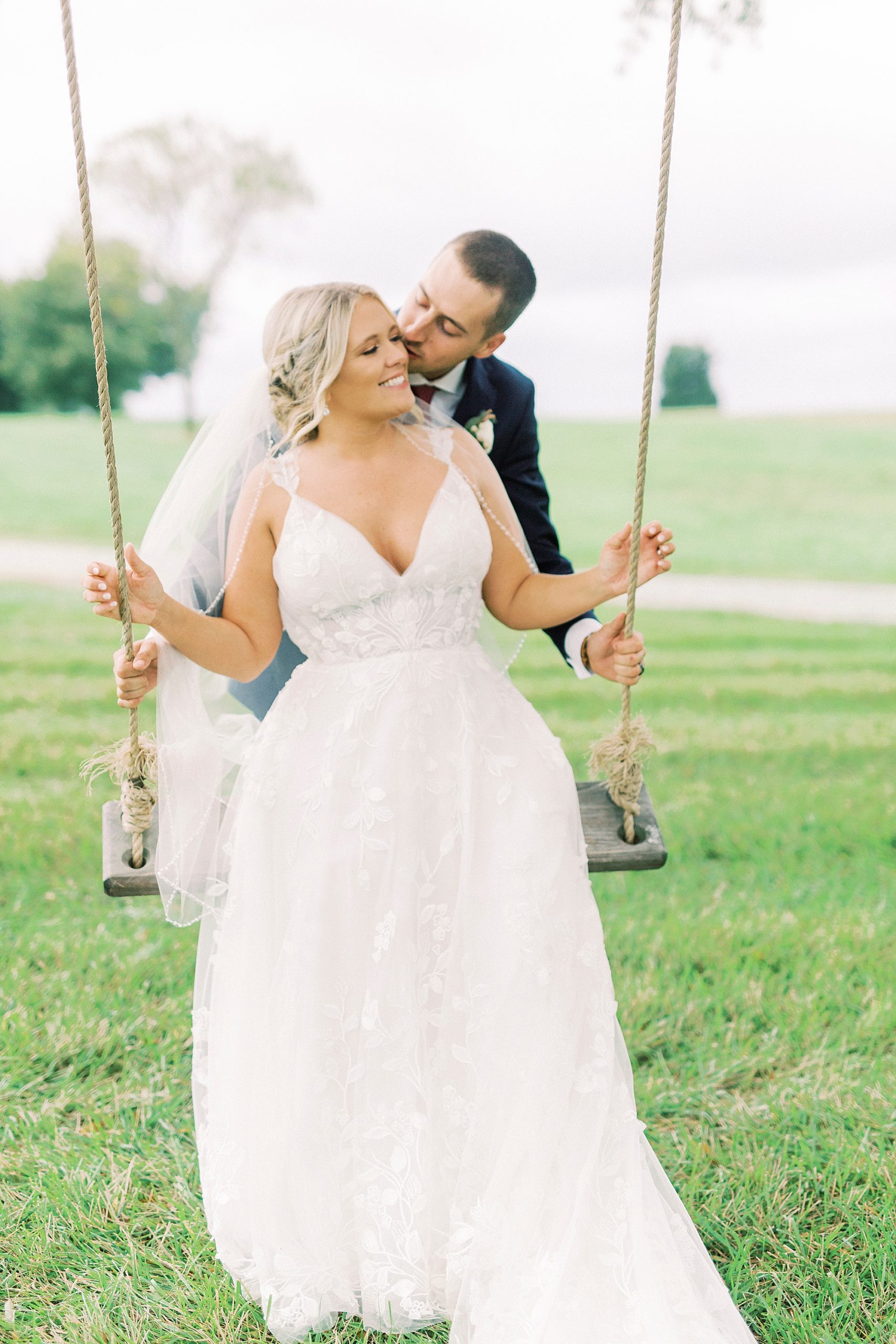 bride swings on wooden swing at Addison Farm with groom behind her