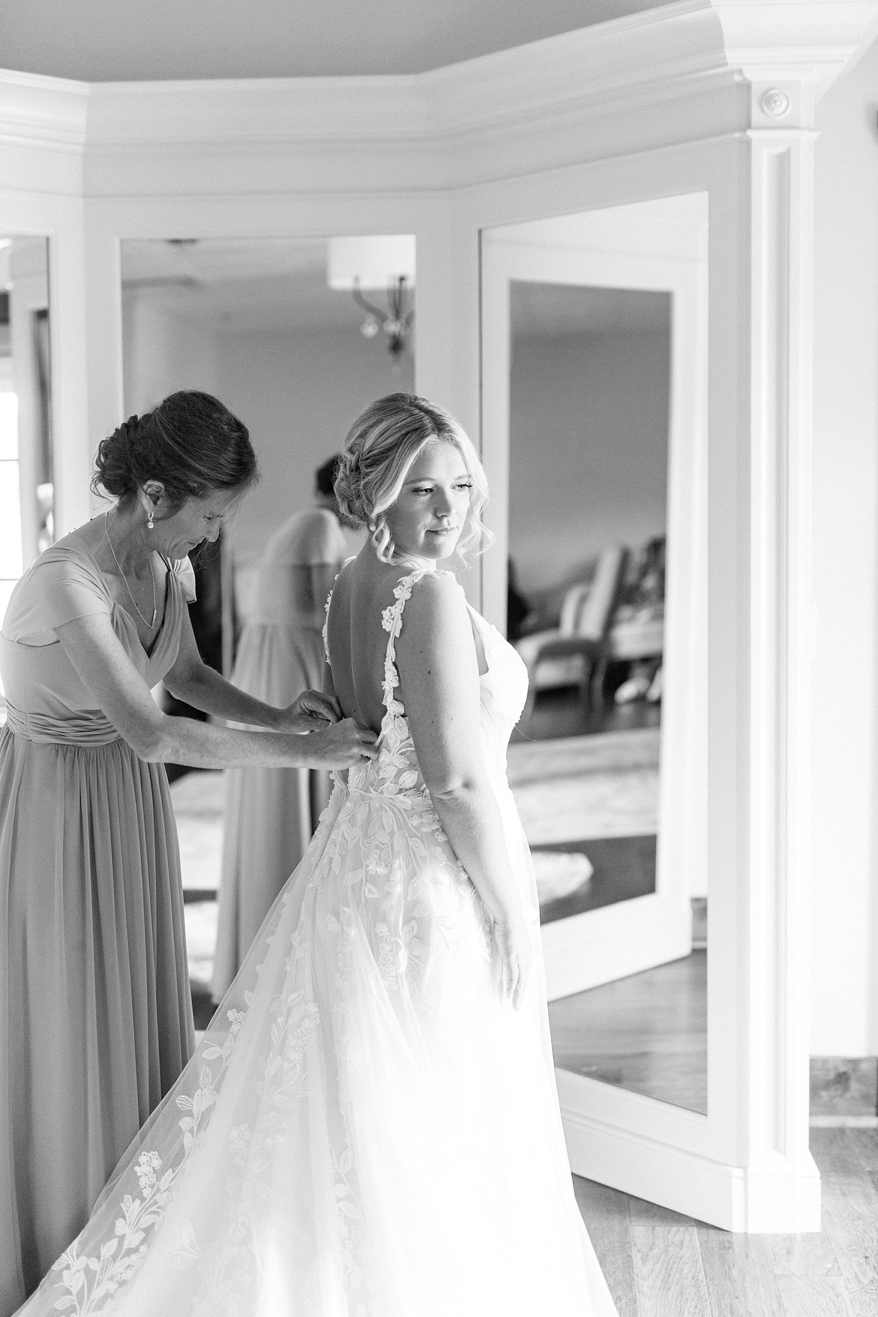 mother helps bride with wedding gown