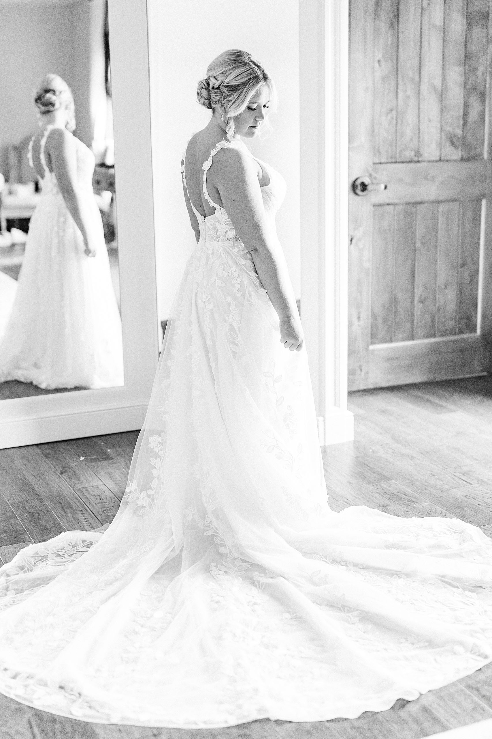 bride stands by mirror looking over shoulder in wedding gown