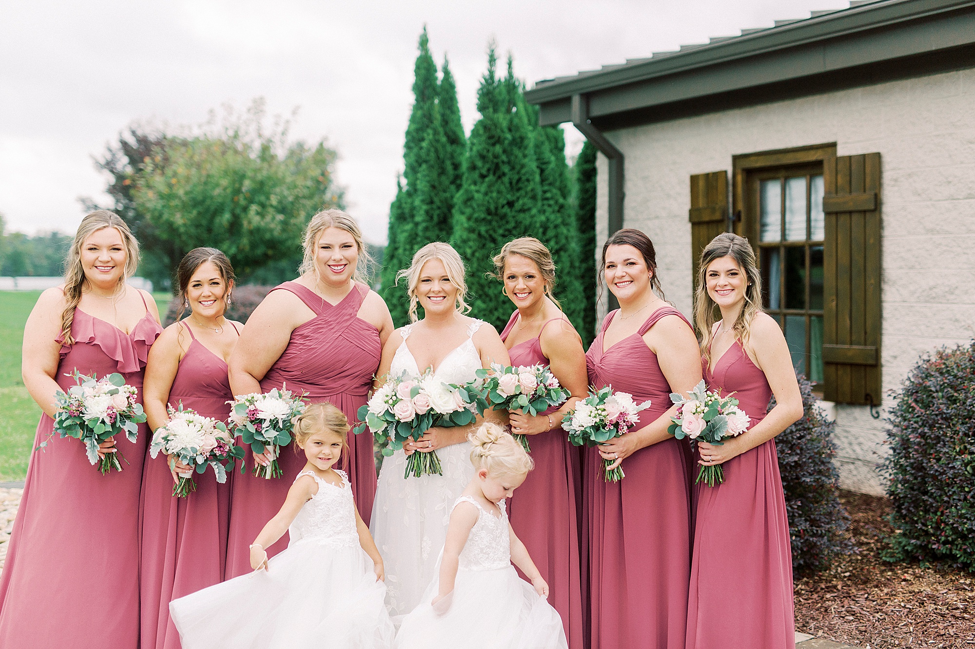 bridesmaids in dark pink gowns smile with bride before NC wedding