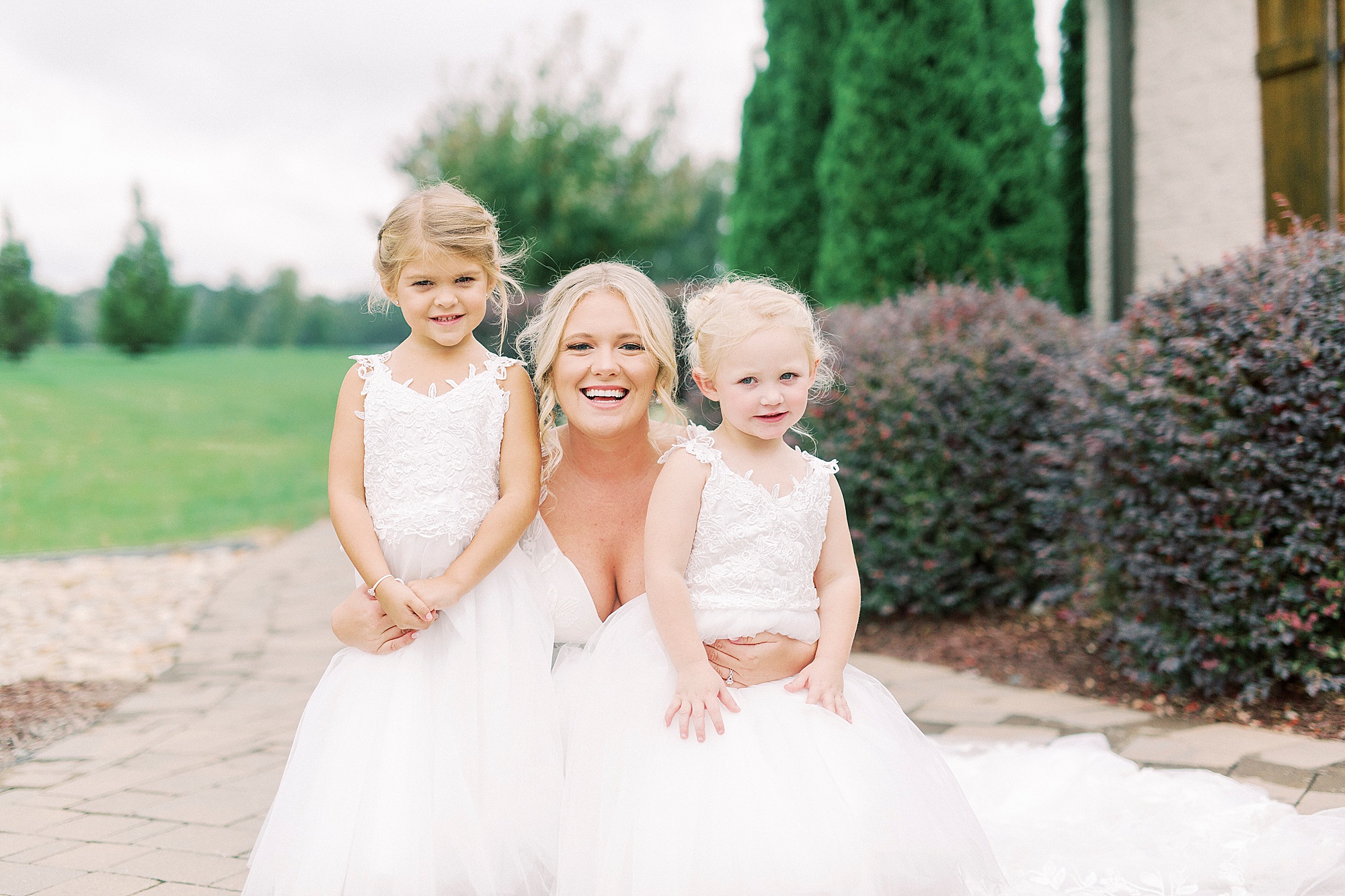 bride kneels with two flower girls on wedding morning