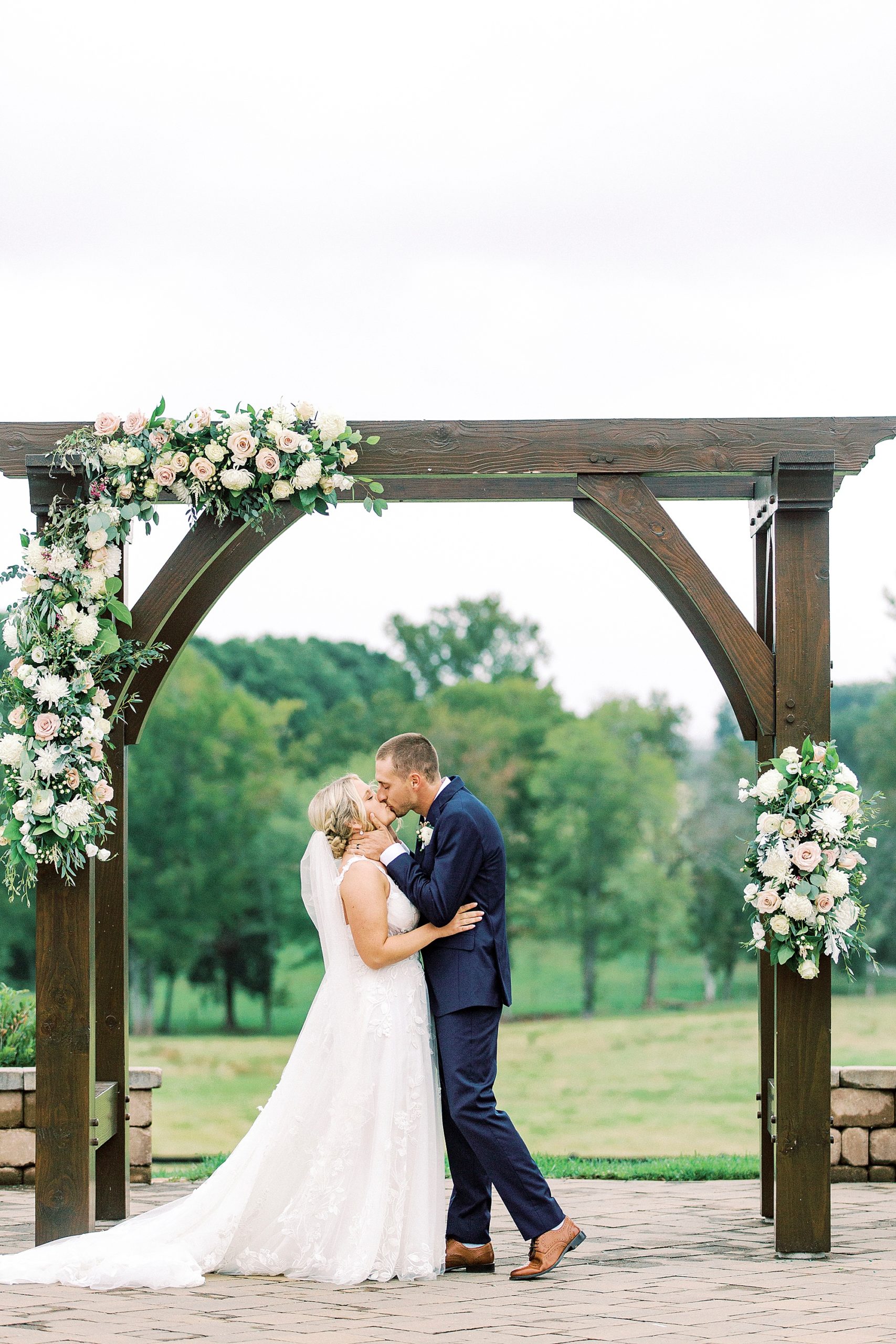 bride and groom kiss under wooden arbor during outdoor ceremony on farm in Greensboro NC