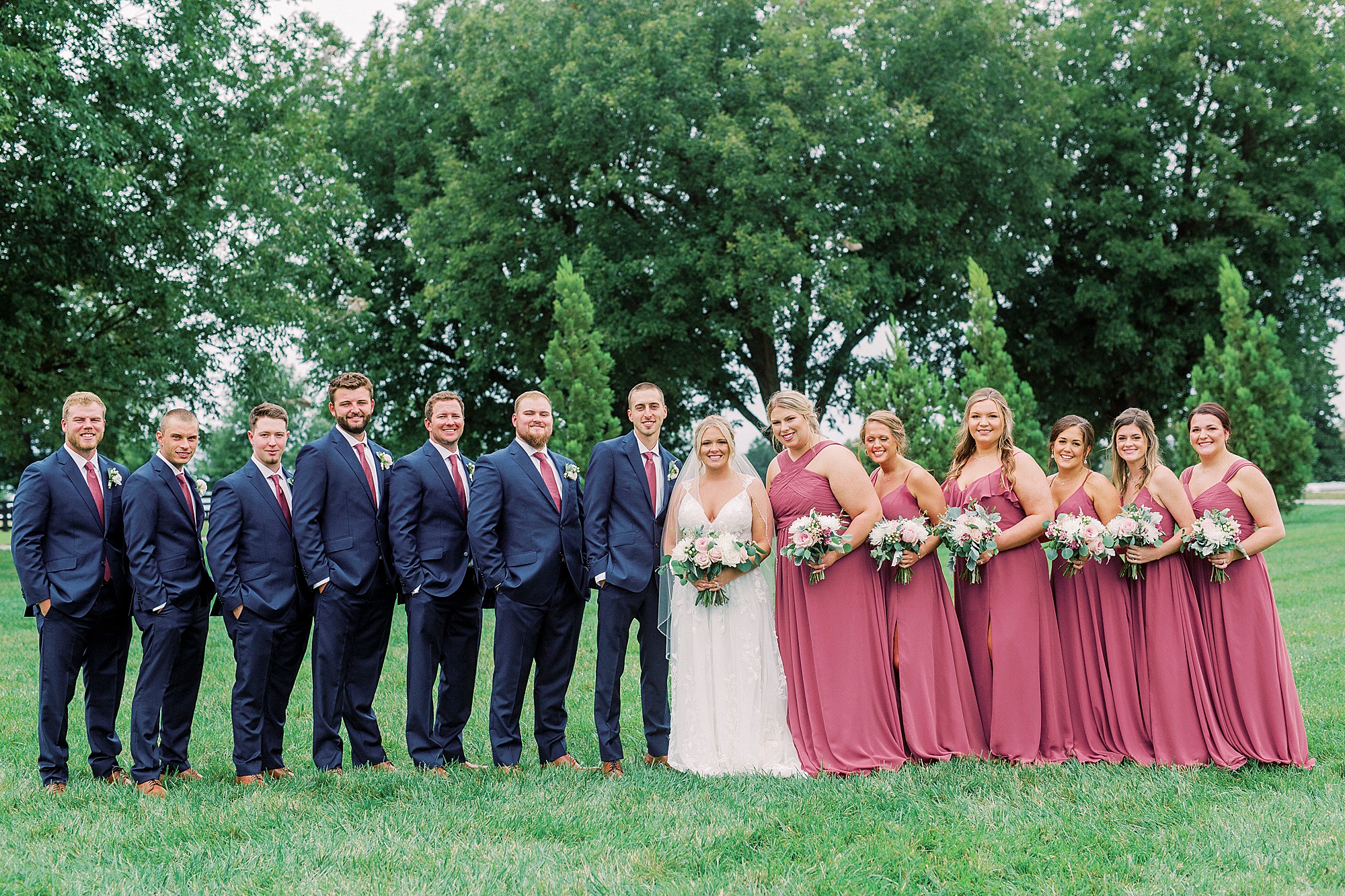 bride and groom pose with wedding party in navy and dark pink