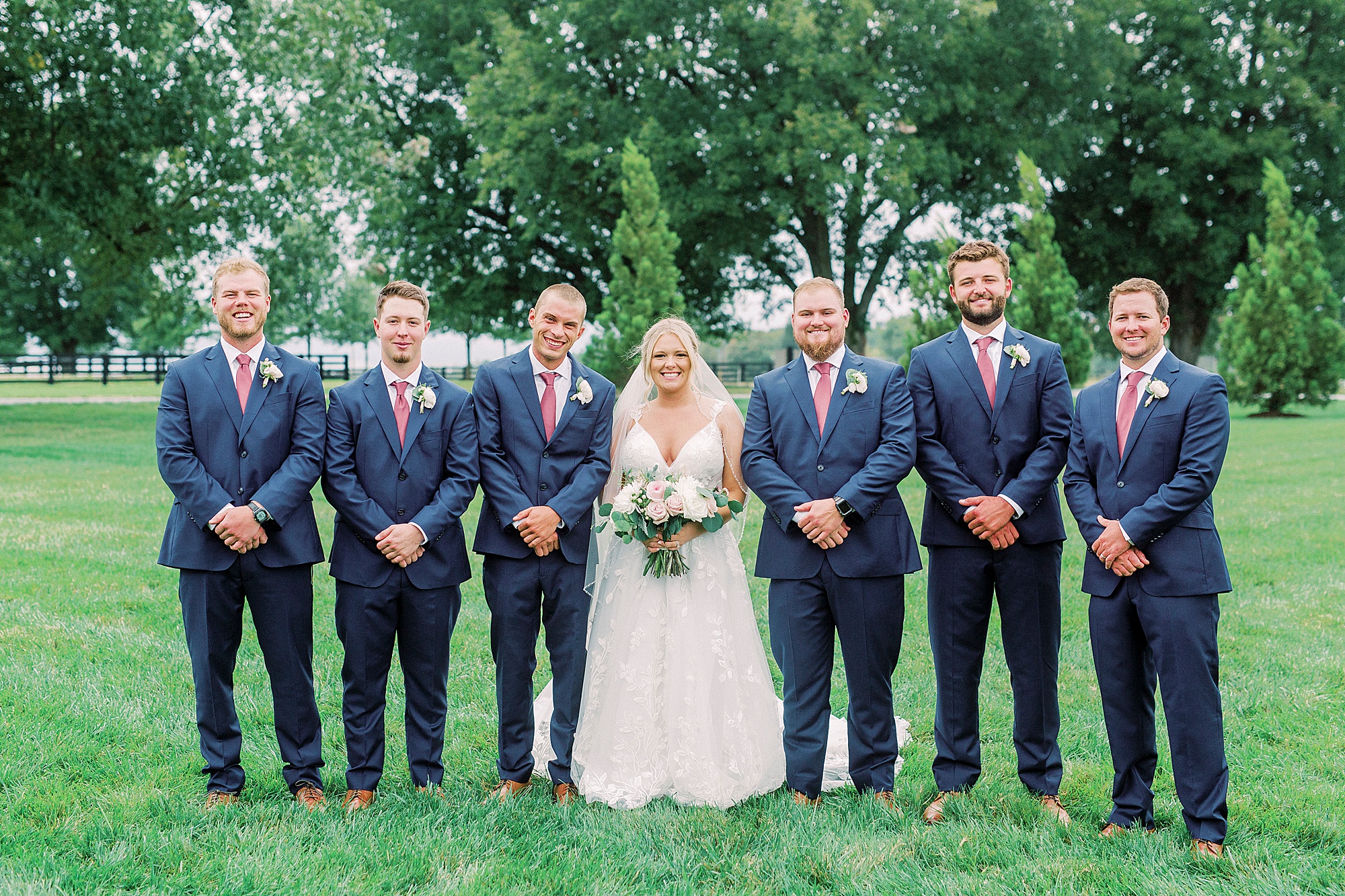 bride stands with groomsmen in navy suits