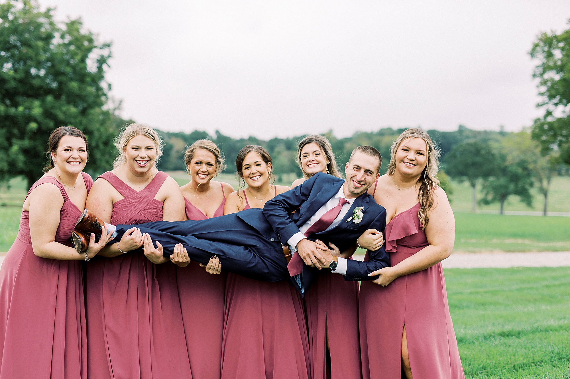 bridesmaids lift groom up during wedding party portraits