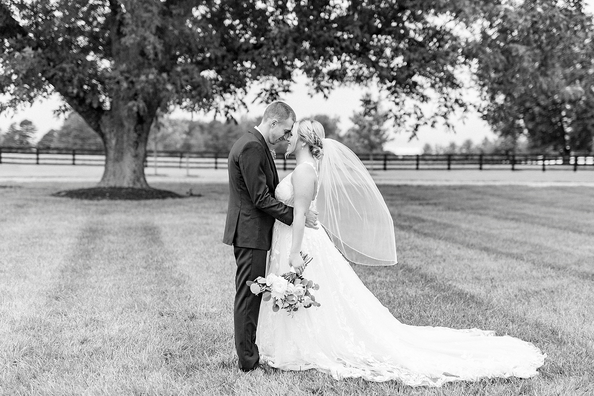 bride and groom hug in field with brides veil floating