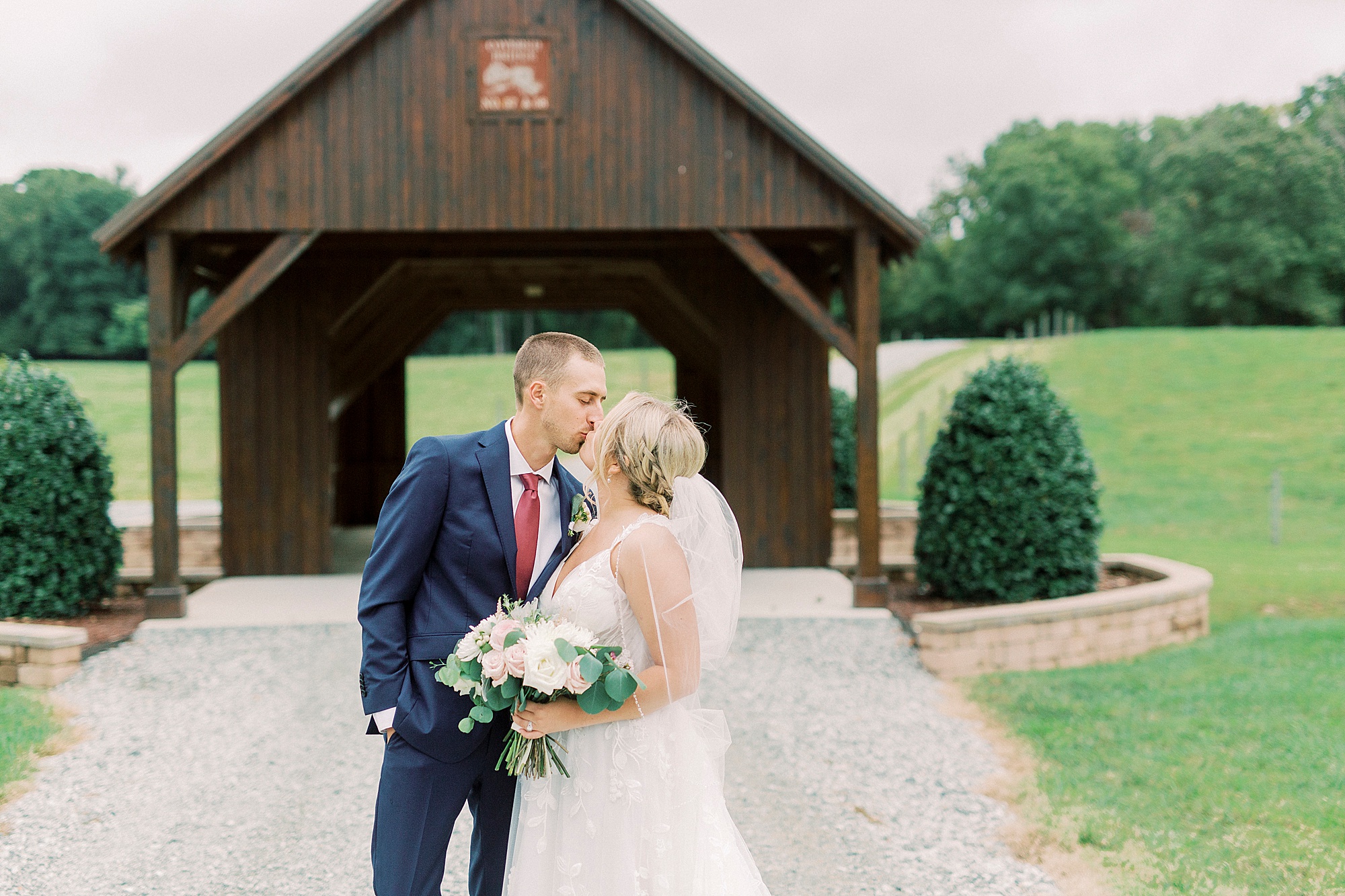 bride and groom kiss by covered barn at Addison Farm