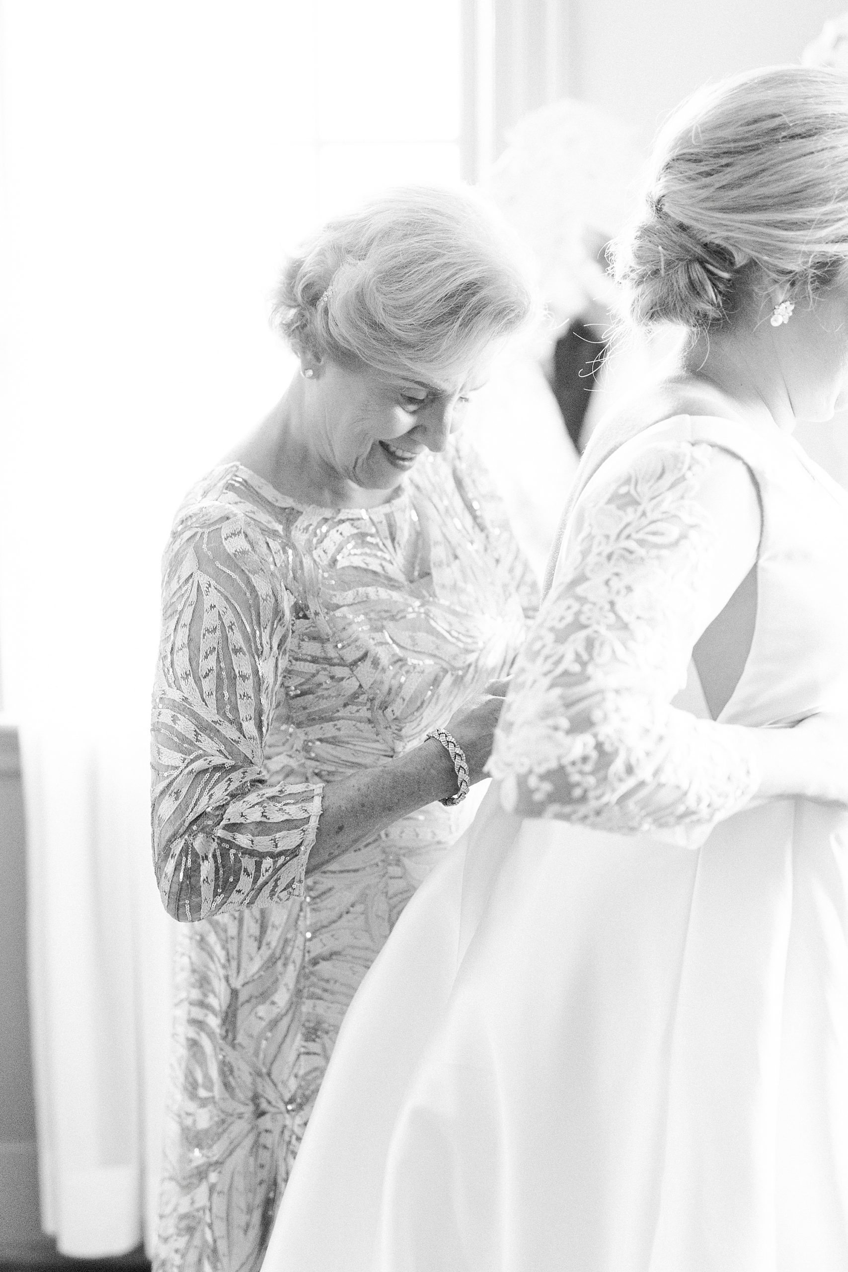 mother helps bride with wedding gown on morning of wedding