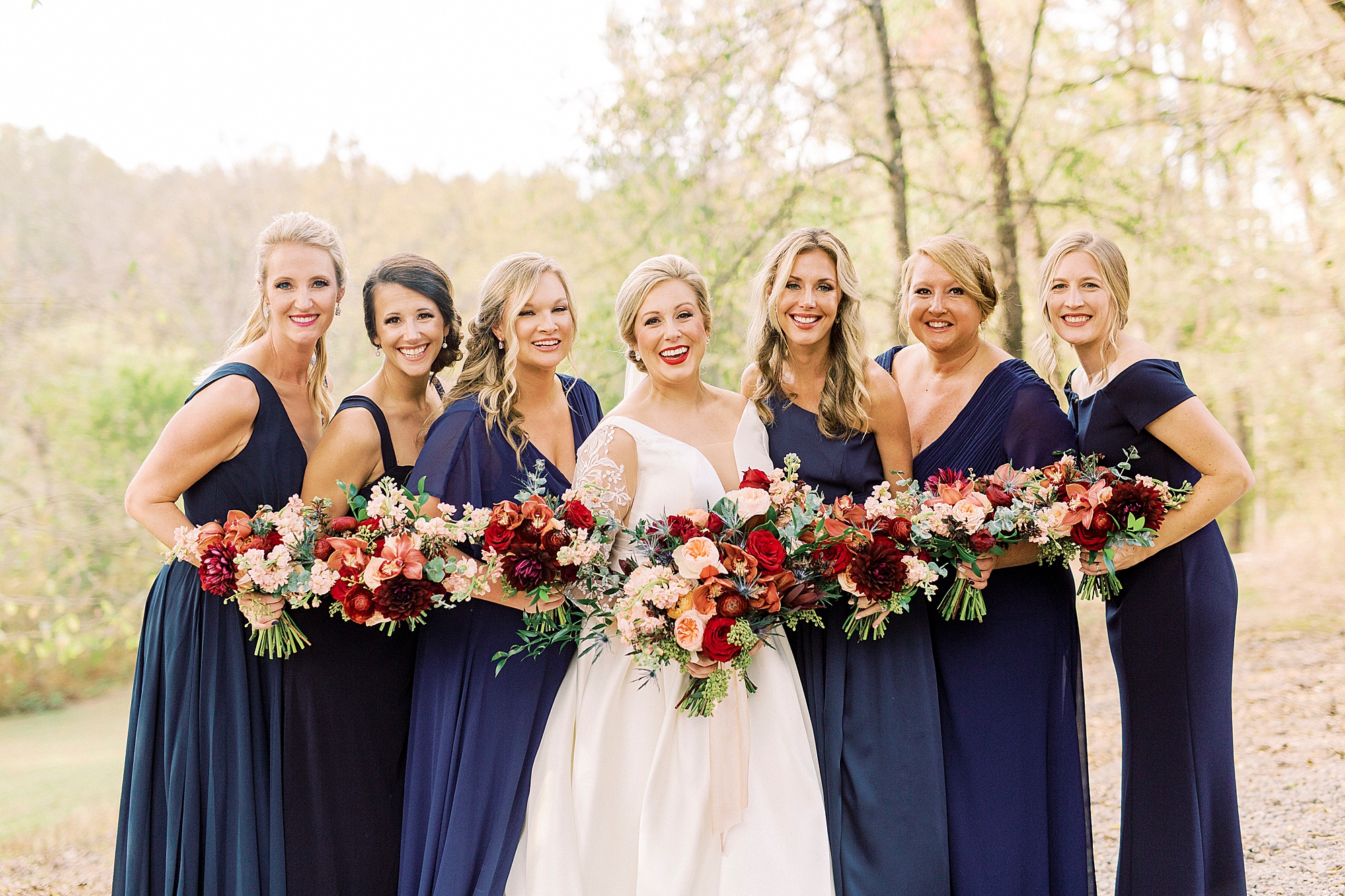 bride poses with bridesmaids in navy blue gowns for fall wedding day