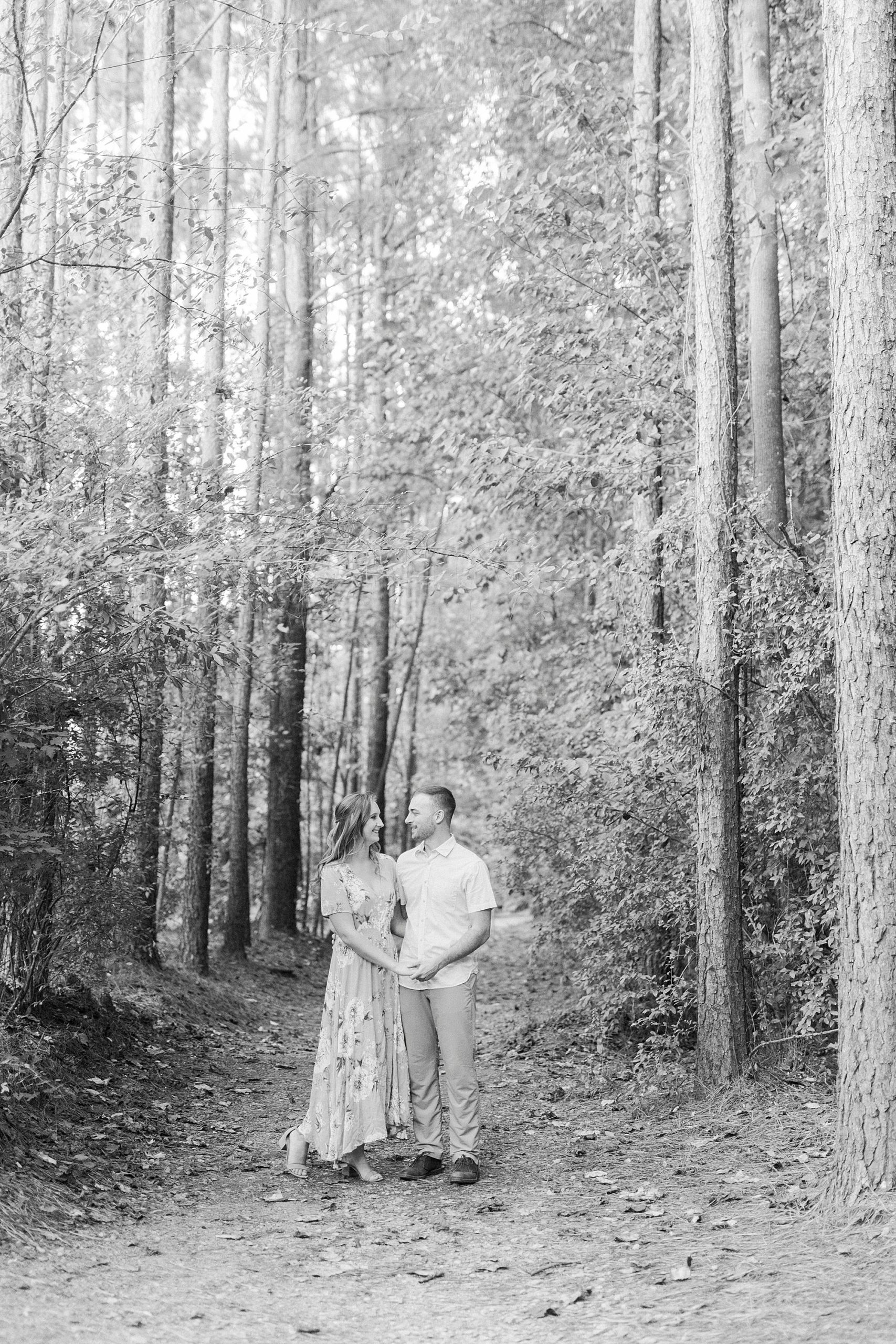 engaged couple stands together between trees at the Whitewater Center