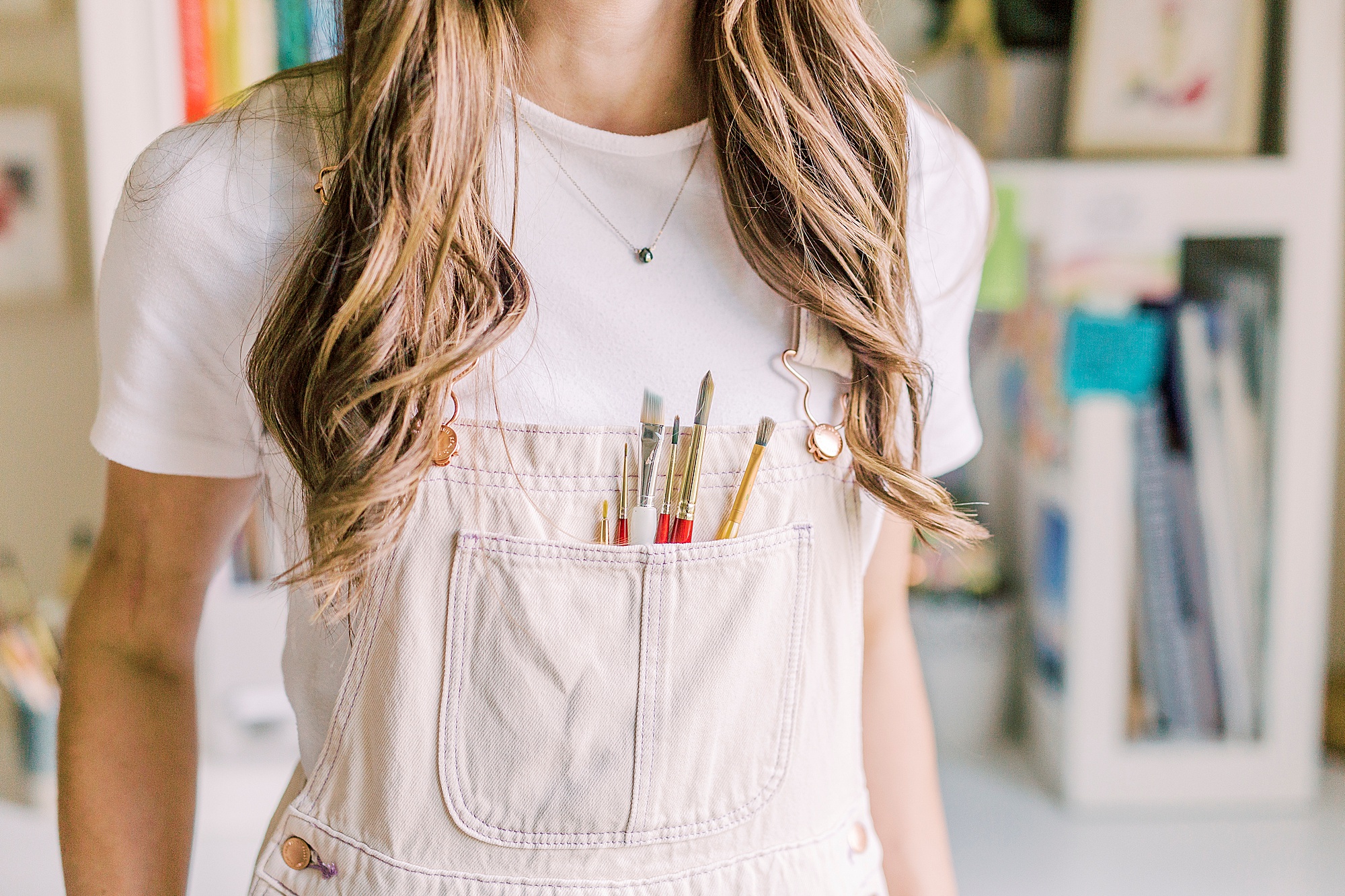 artist holds watercolor brushes in overall pockets