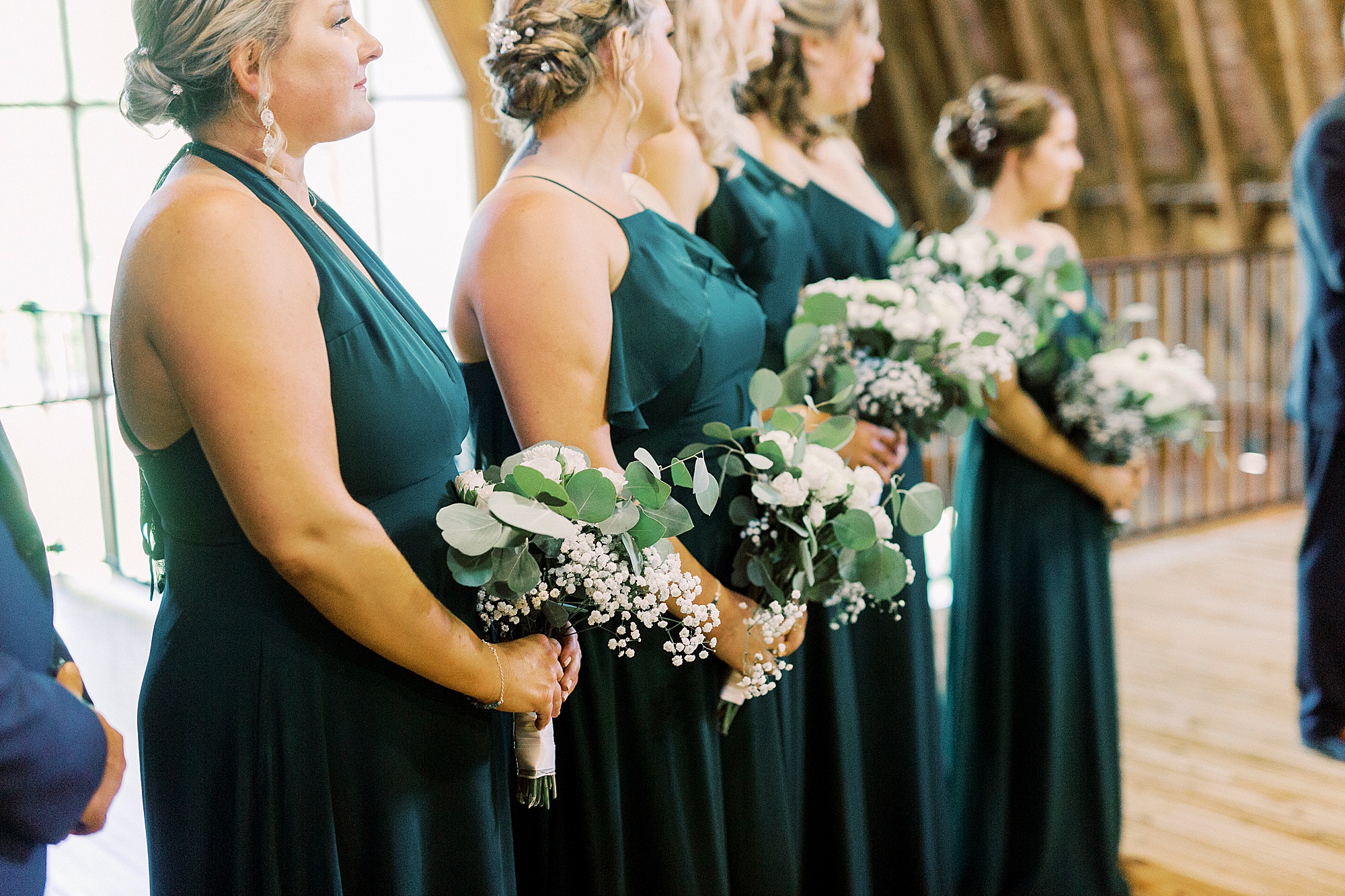 bridesmaids in emerald gren gowns hold bouquets during ceremony