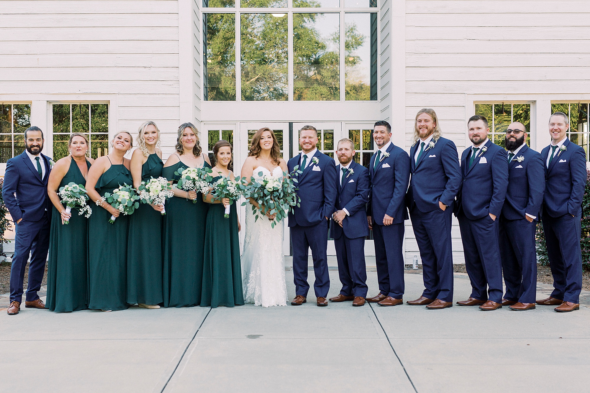 bride and groom pose with wedding party in emerald and navy attire