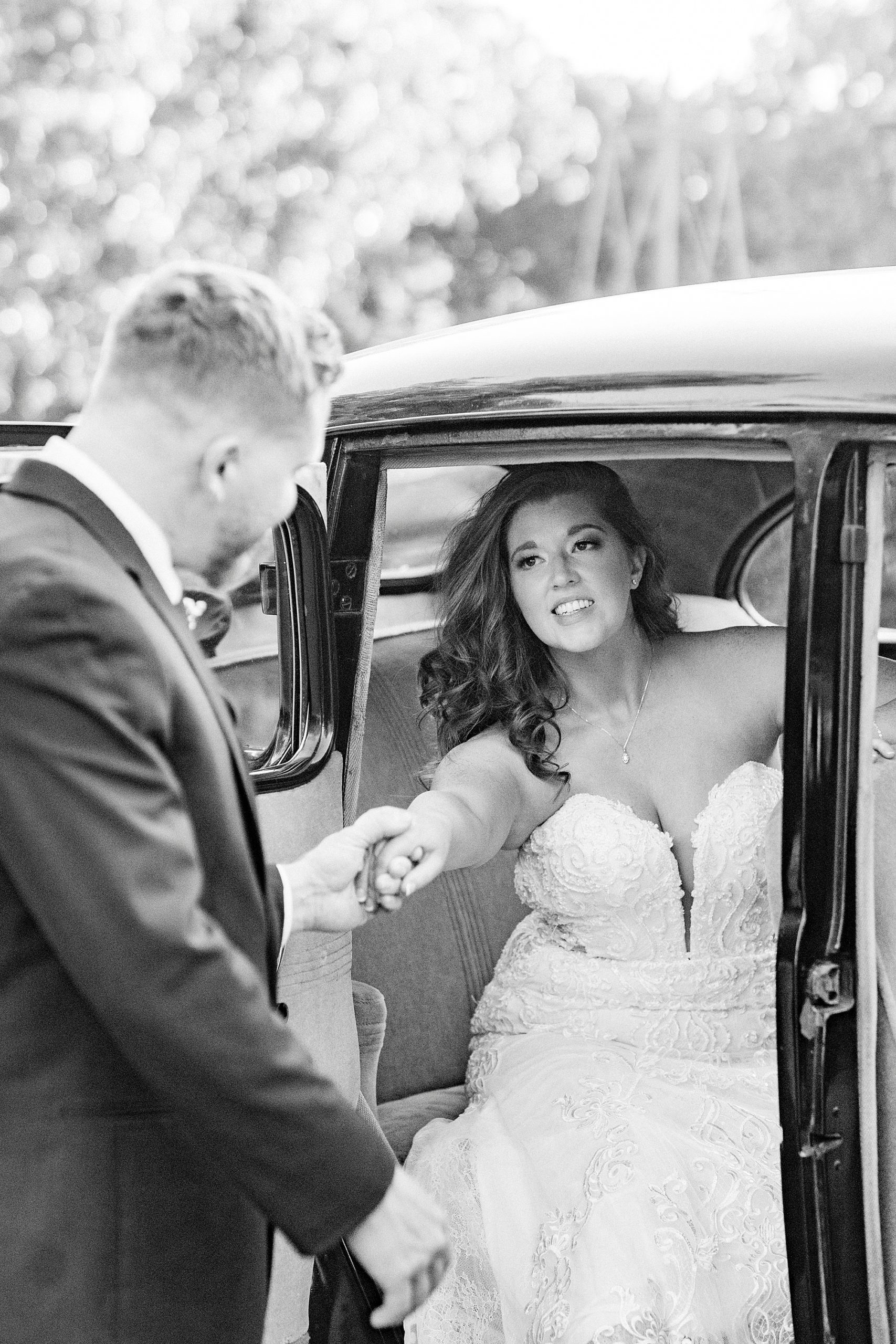 groom helps bride out of car during wedding portraits