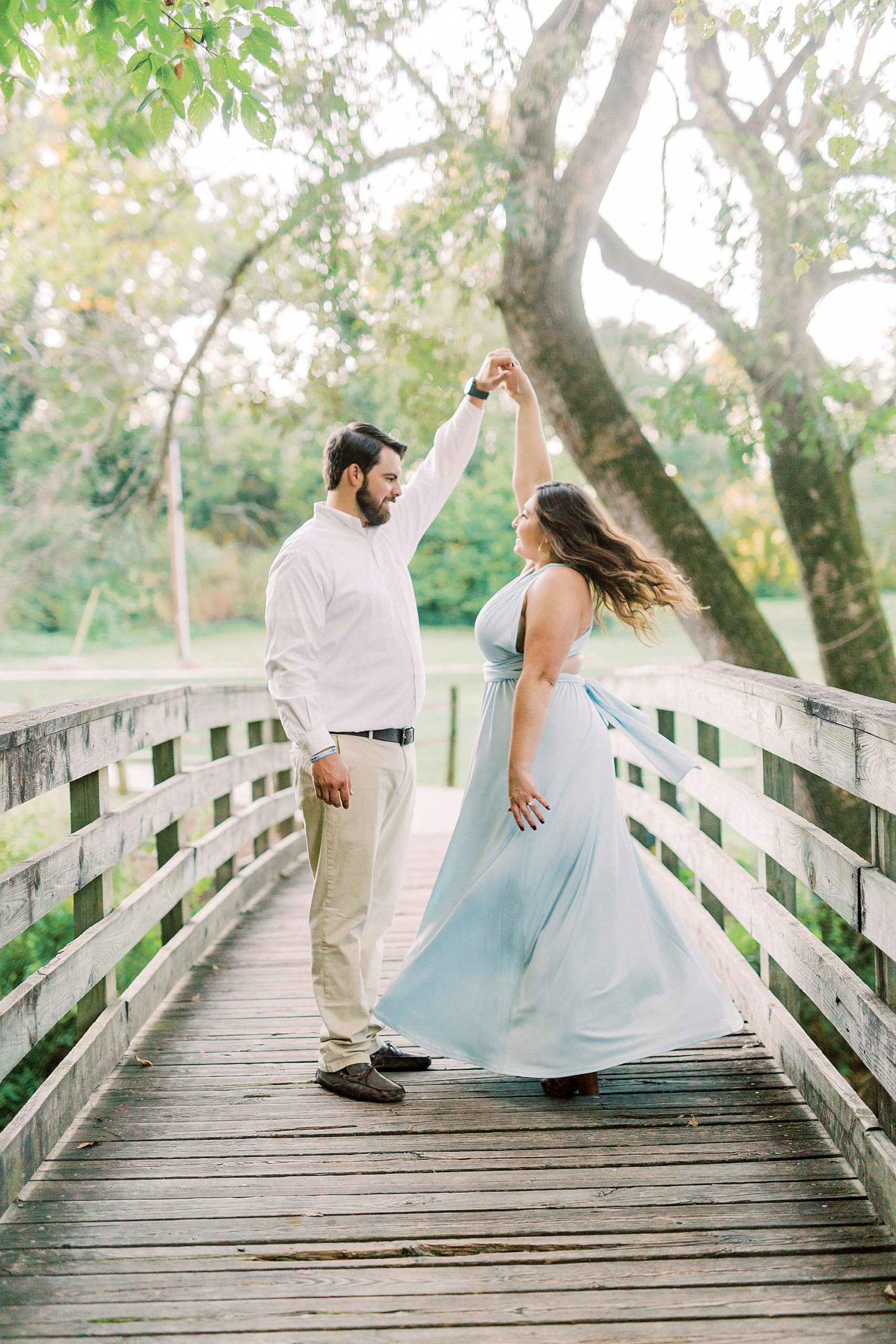 groom twirls bride in blue dress on wooden bridge