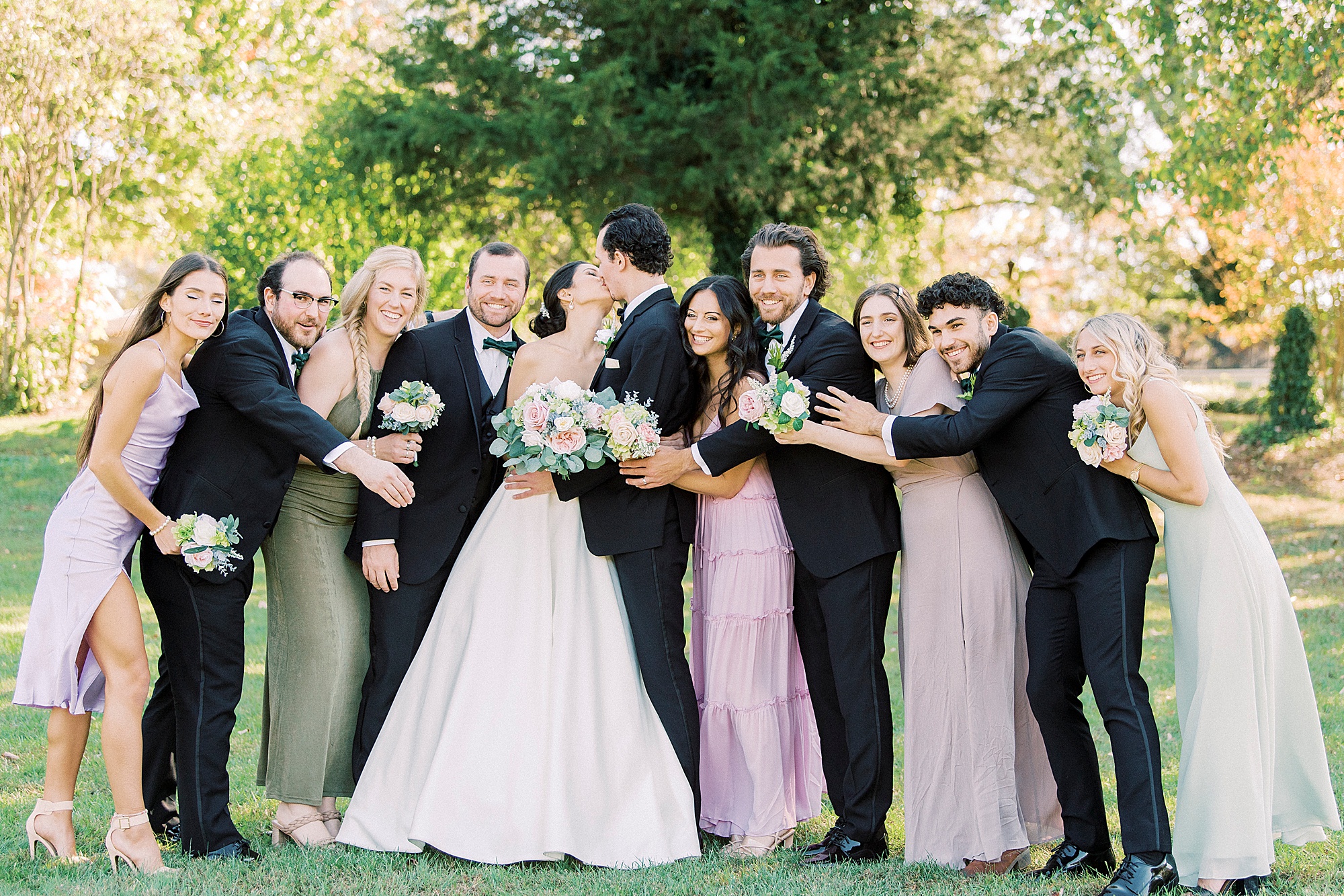 bride and groom kiss while wedding party hugs them
