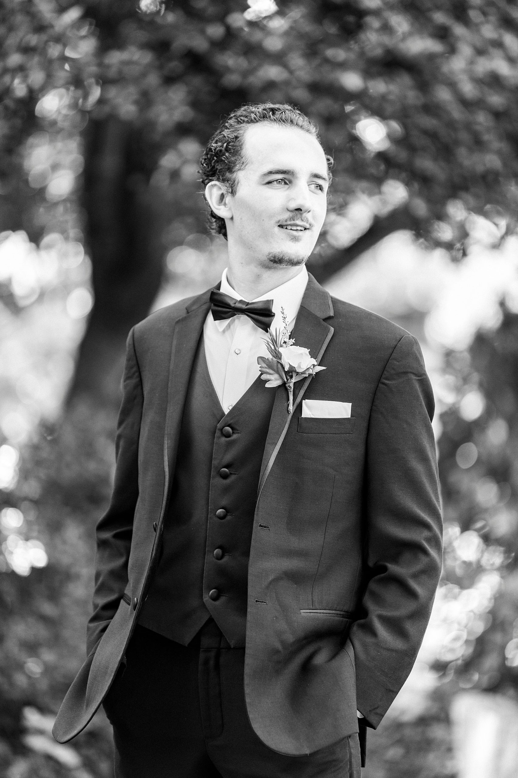 groom poses with hands in pocket of classic black suit