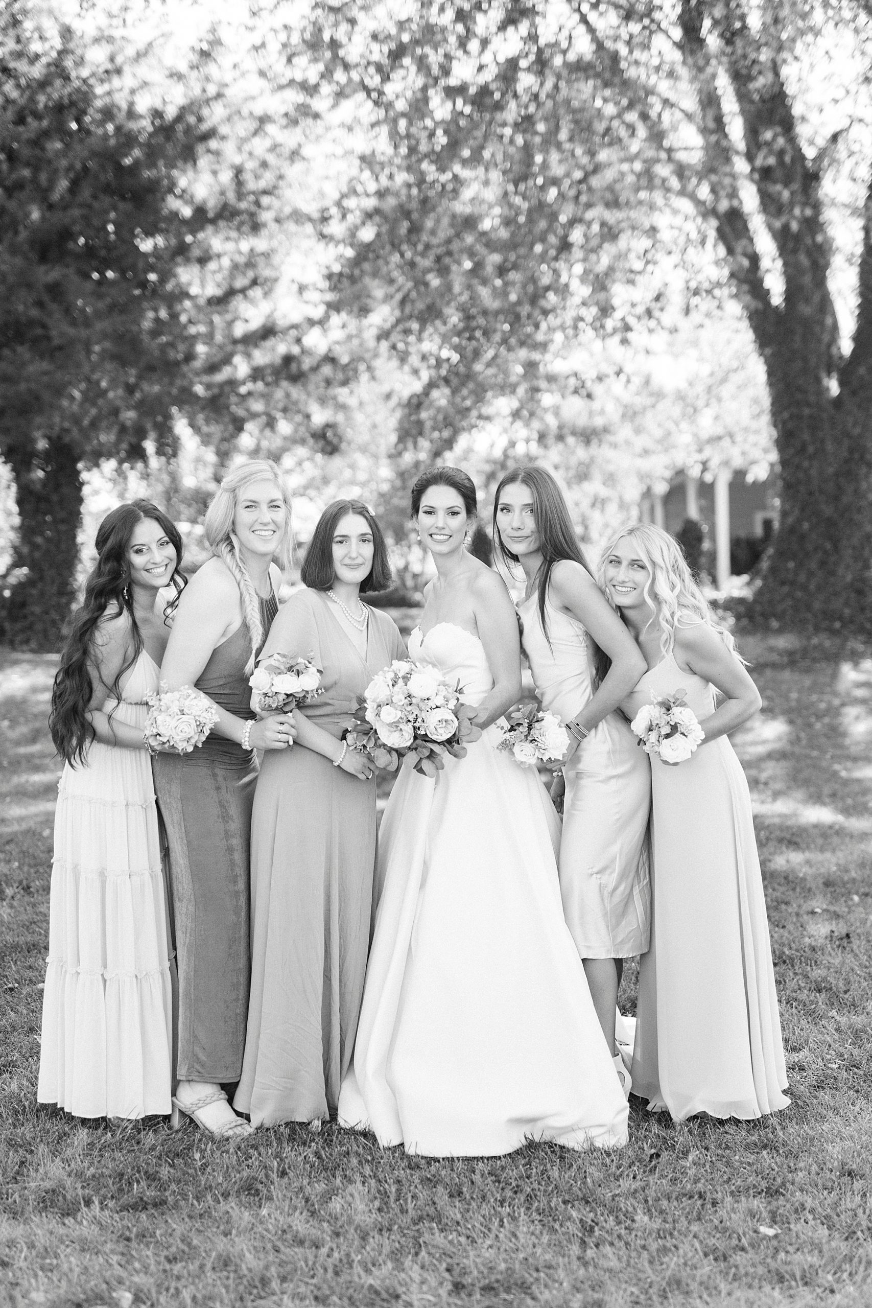 bride and bridesmaids stand together under trees at 1812 Hitching Post