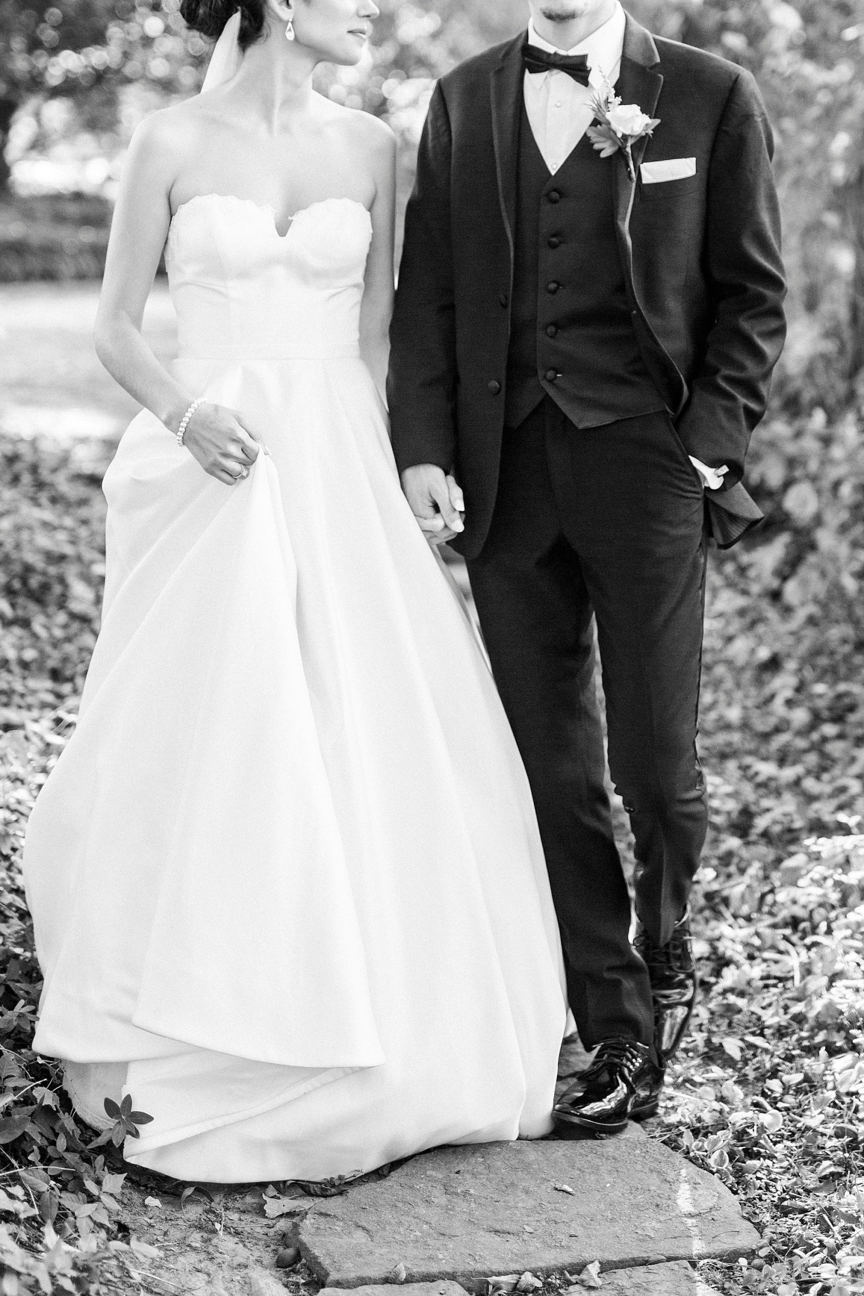 couple holds hands walking on pathway during 1812 Hitching Post wedding portraits