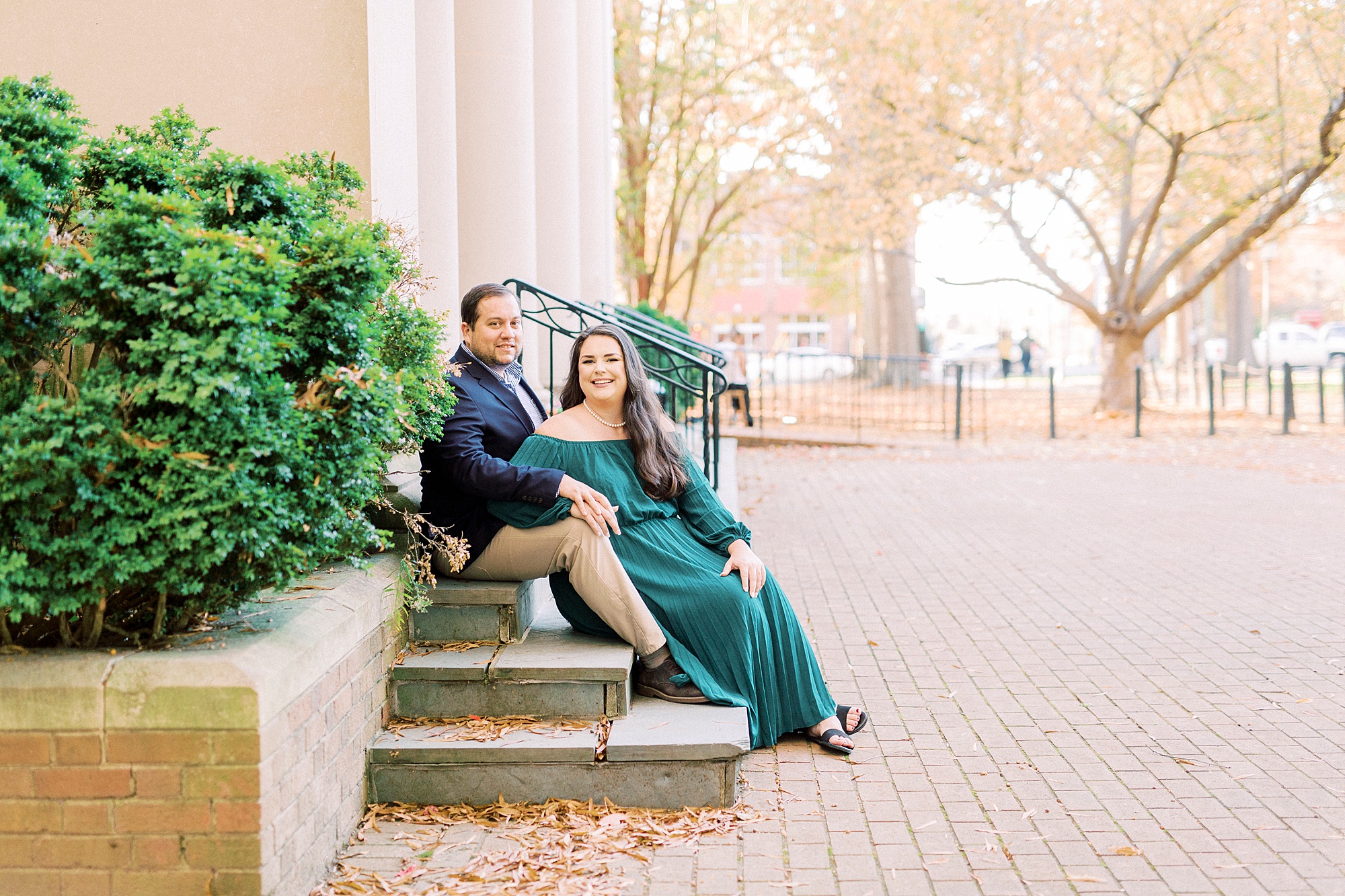 couple sits on steps during fall engagement photos in Downtown Davidson NC