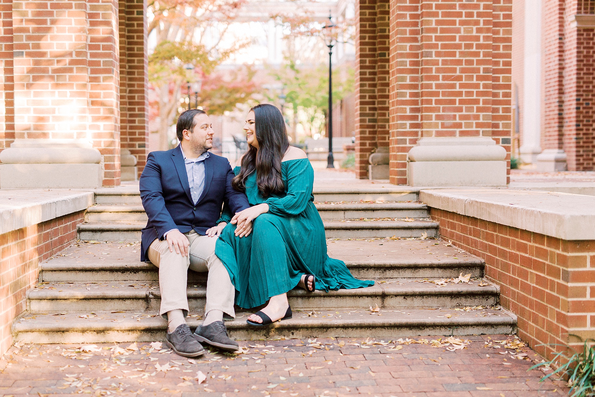 engaged couple sits on brick steps in Downtown Davidson during fall engagement photos