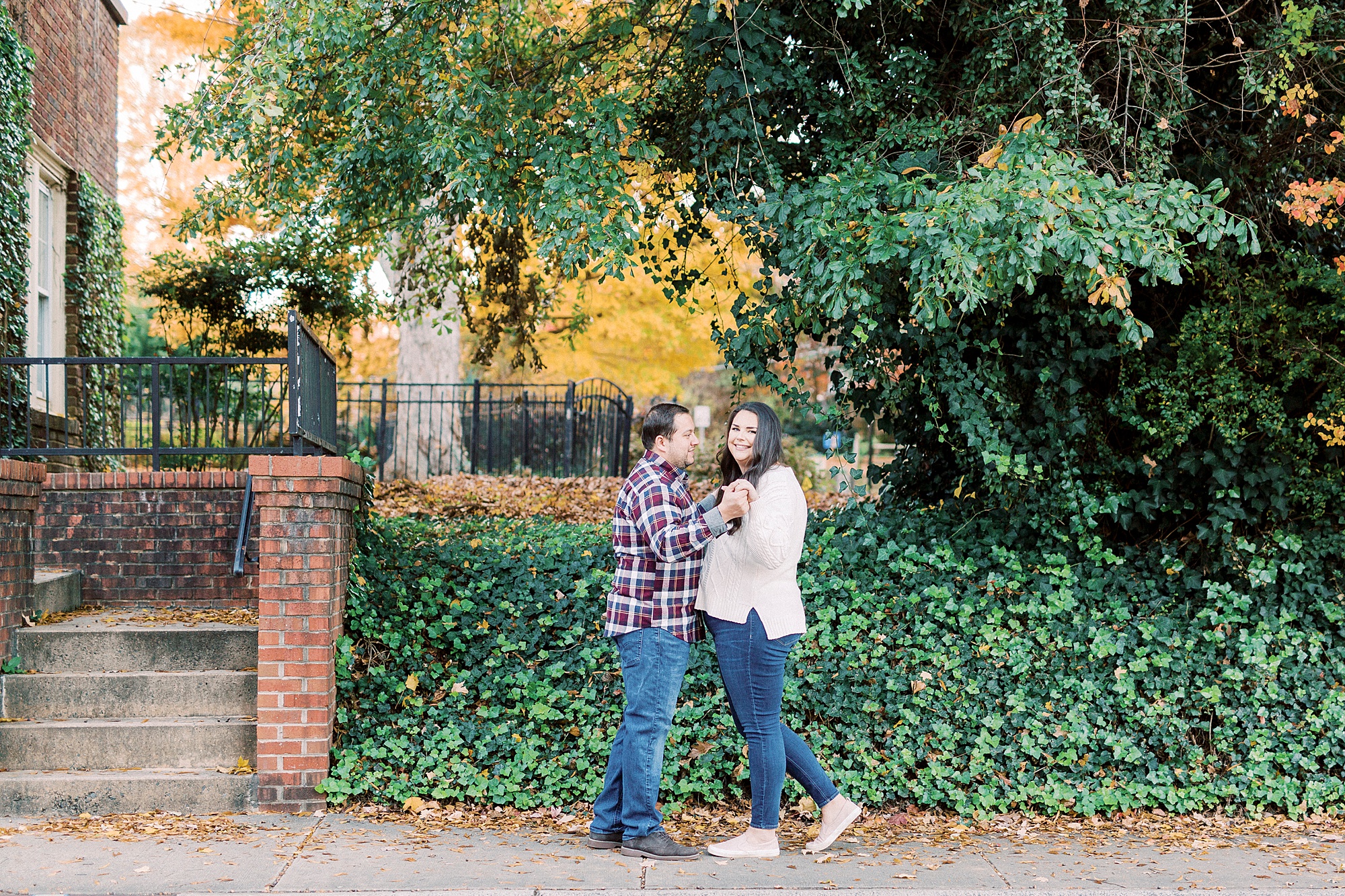 engaged couple holds hands by bushes in Downtown Davidson