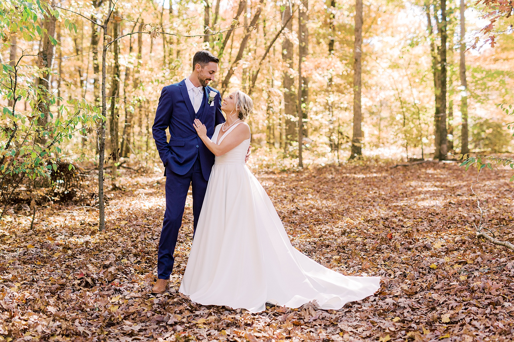 newlyweds stand in fallen leaves during portraits at the Farm at Brusharbor