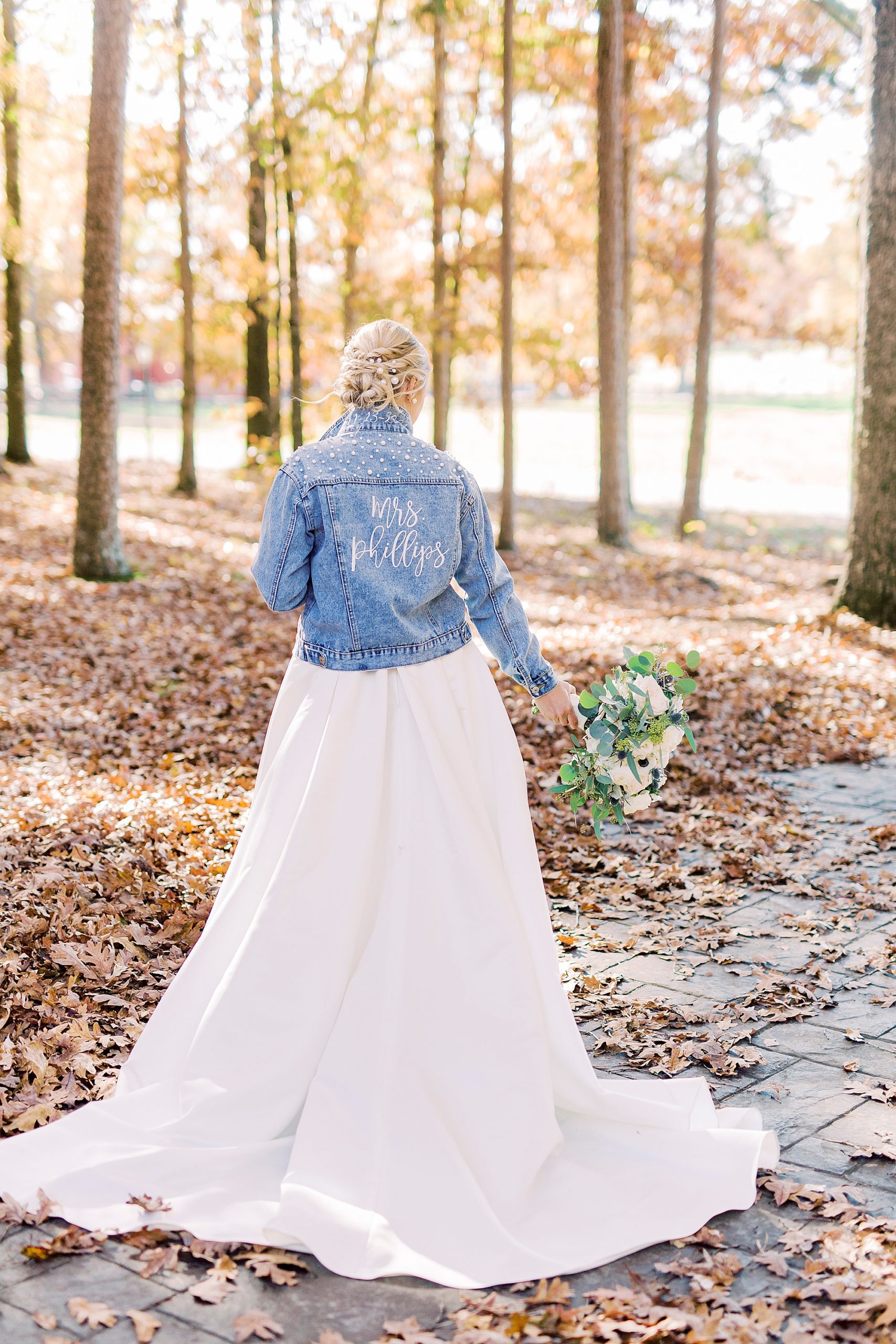 bride poses with jean jacket over wedding gown in woods at the Farm at Brusharbor