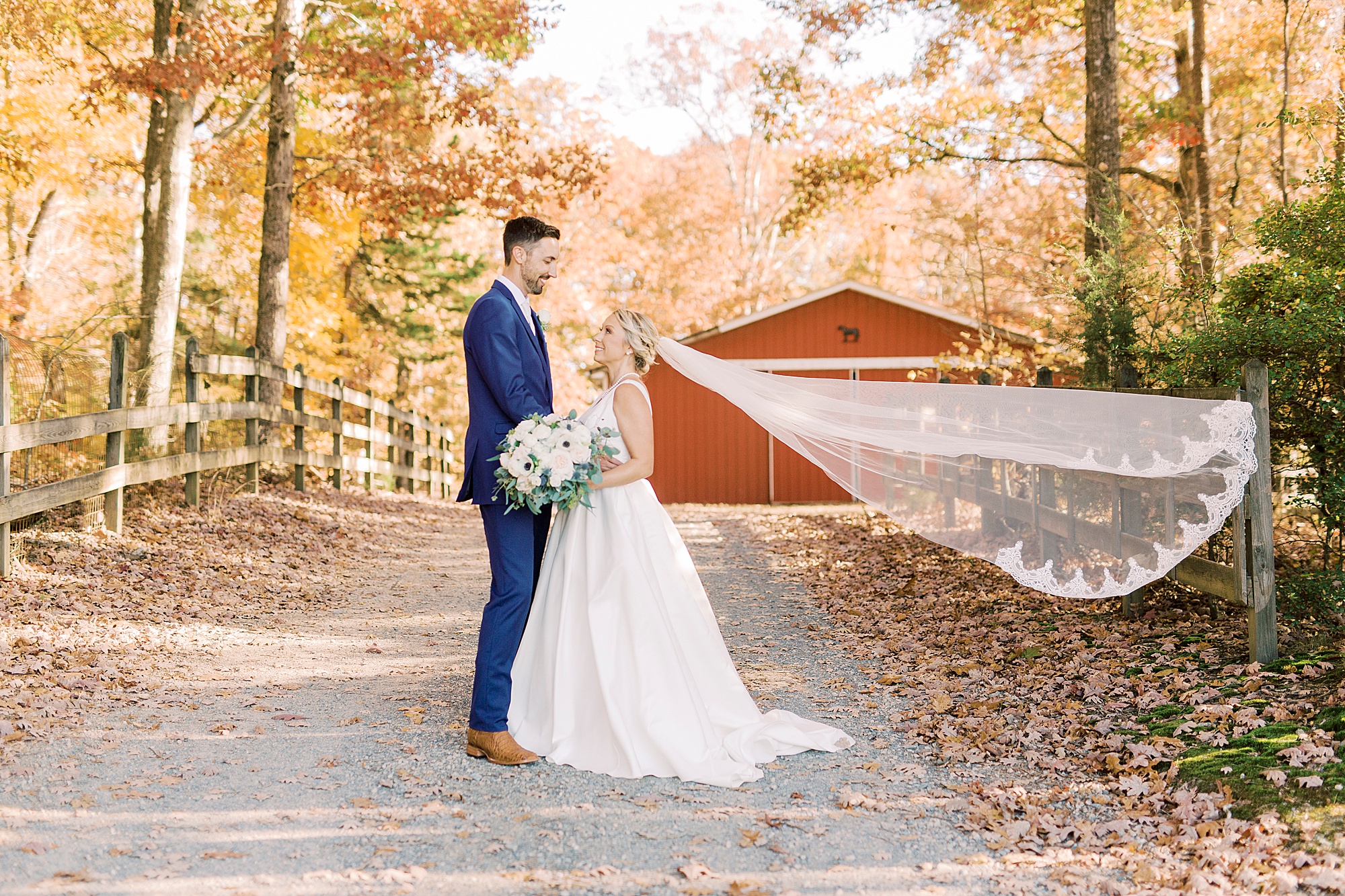 bride and groom hug outside red barn during fall wedding at the Farm at Brusharbor