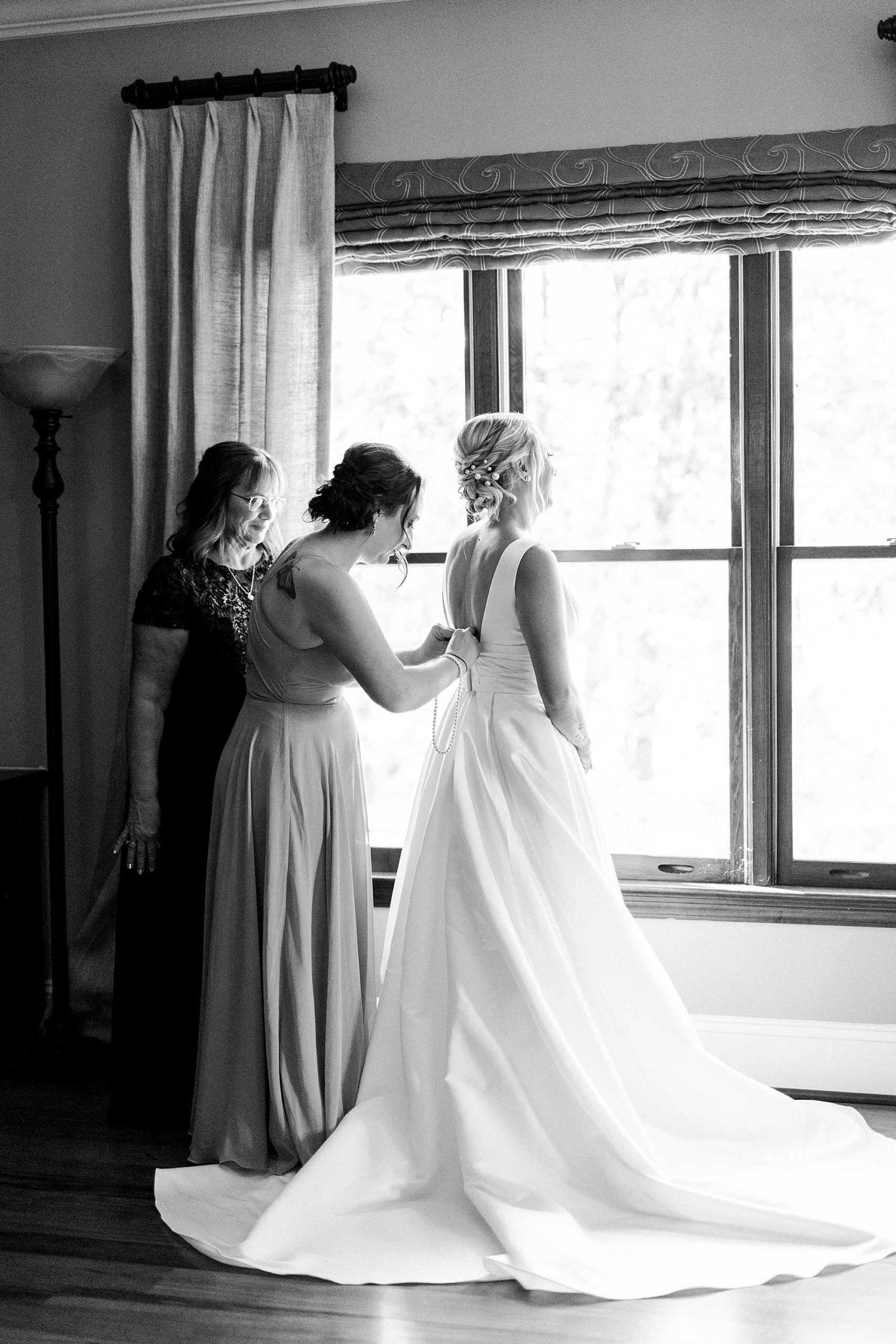 bridesmaid helps bride with wedding gown before NC wedding