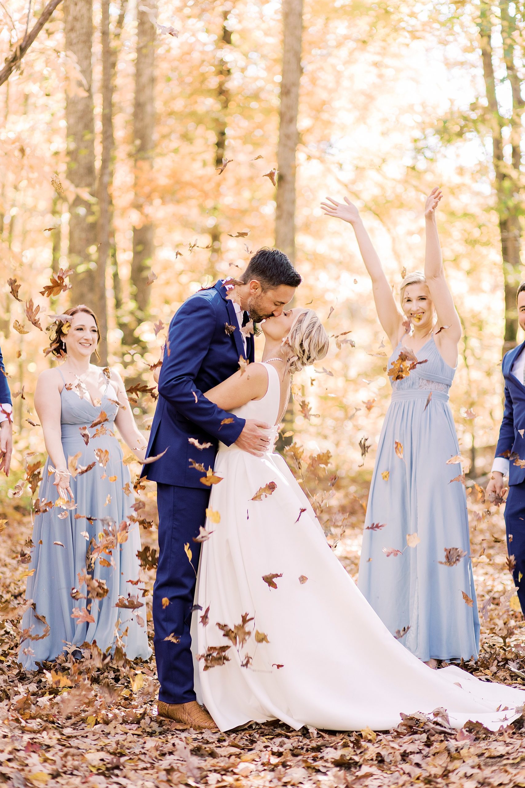 couple kisses while bridal party throws fall leaves