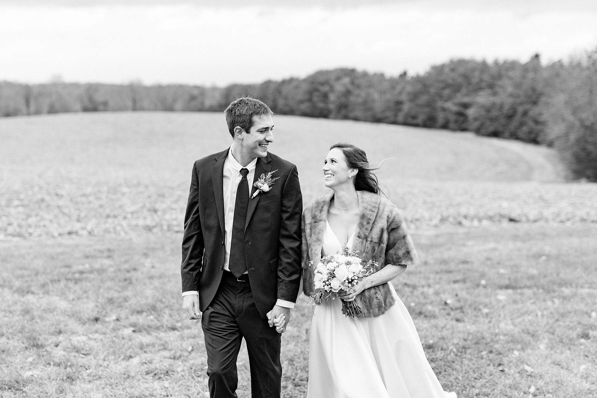 bride and groom hold hands walking near field