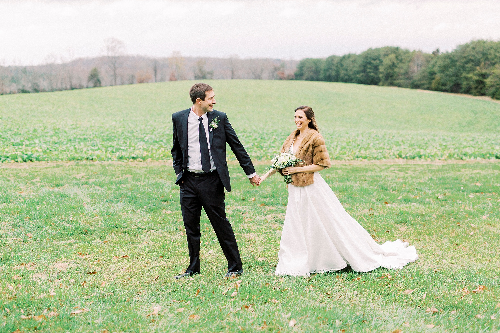 newlyweds hold hands walking through field for winter wedding
