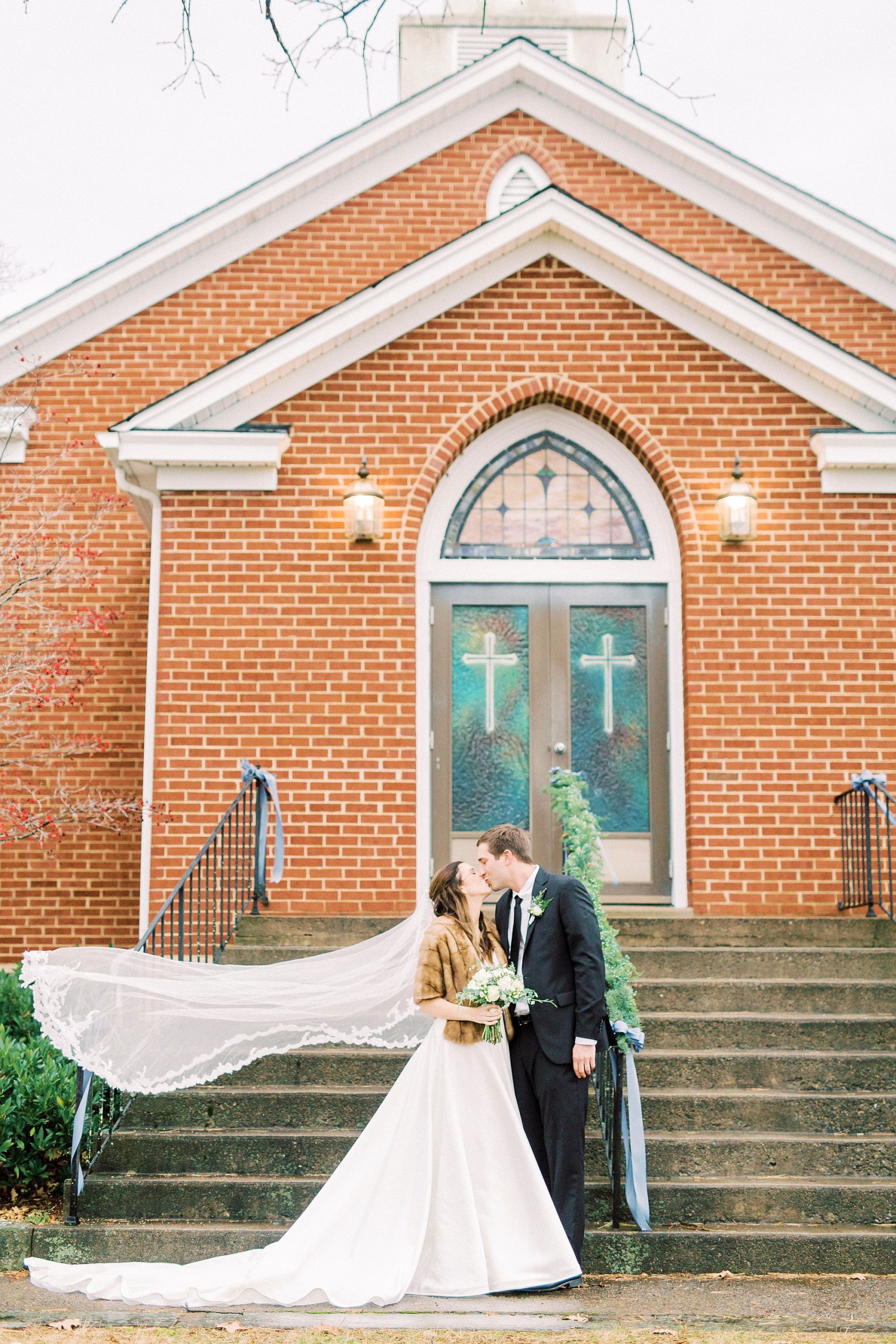 bride and groom kiss outside Bethesda United Methodist Church with bride's veil floating