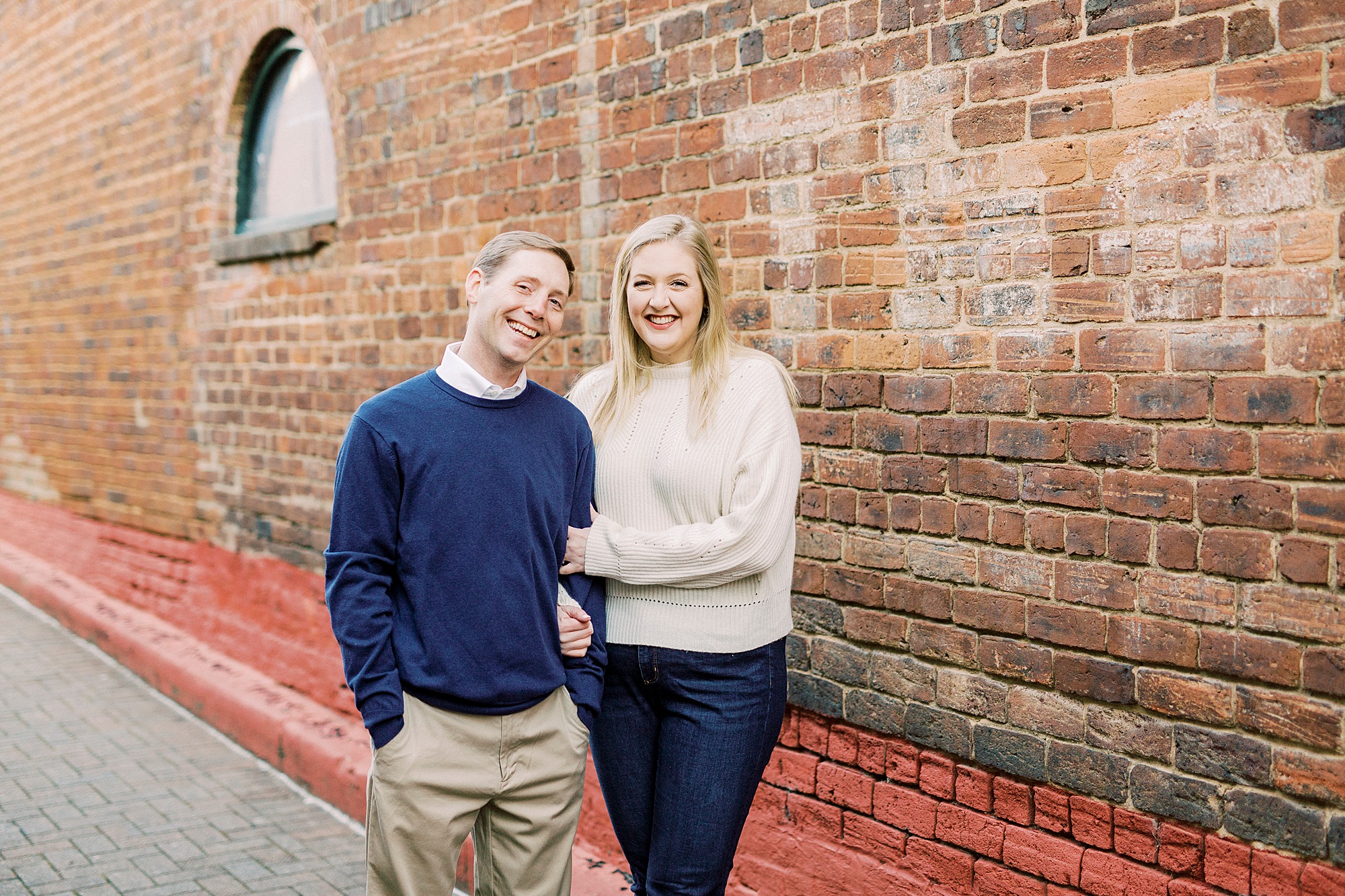 engaged couple poses along brick wall in Downtown Concord