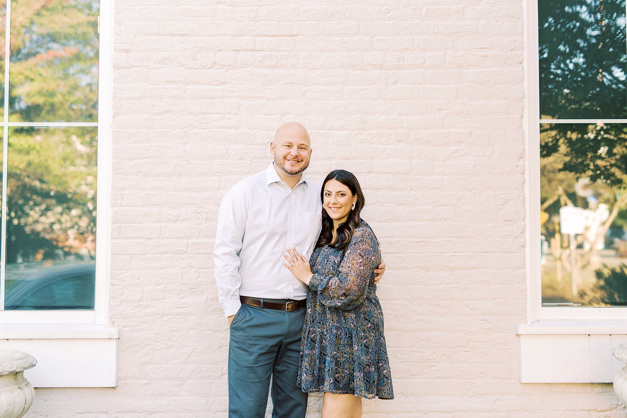 engaged couple poses against pale pink wall in Matthews NC