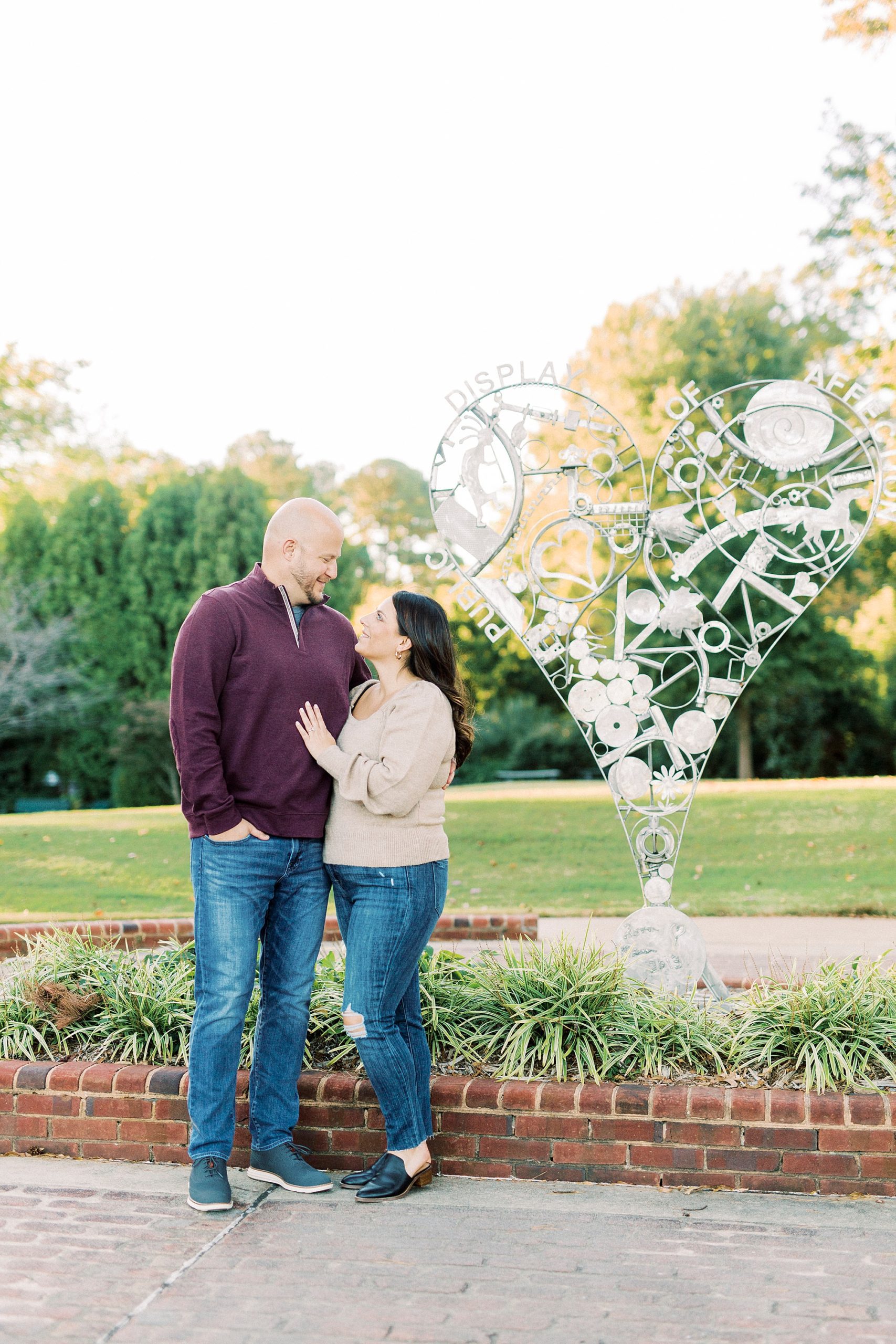 bride and groom pose by heart statue during Downtown Matthews engagement session