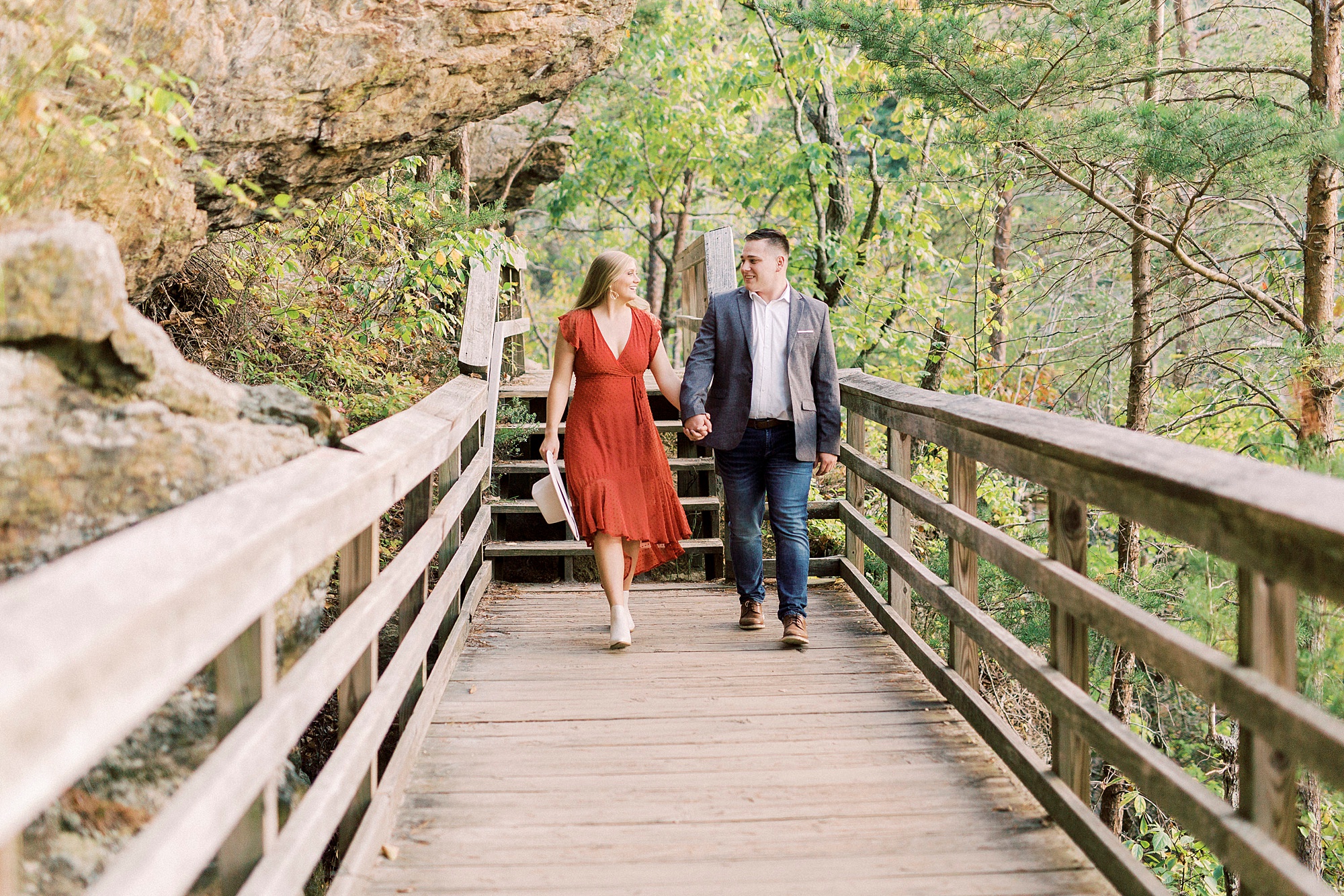 couple holds hands walking on wooden bridge in Hanging Rock State Park