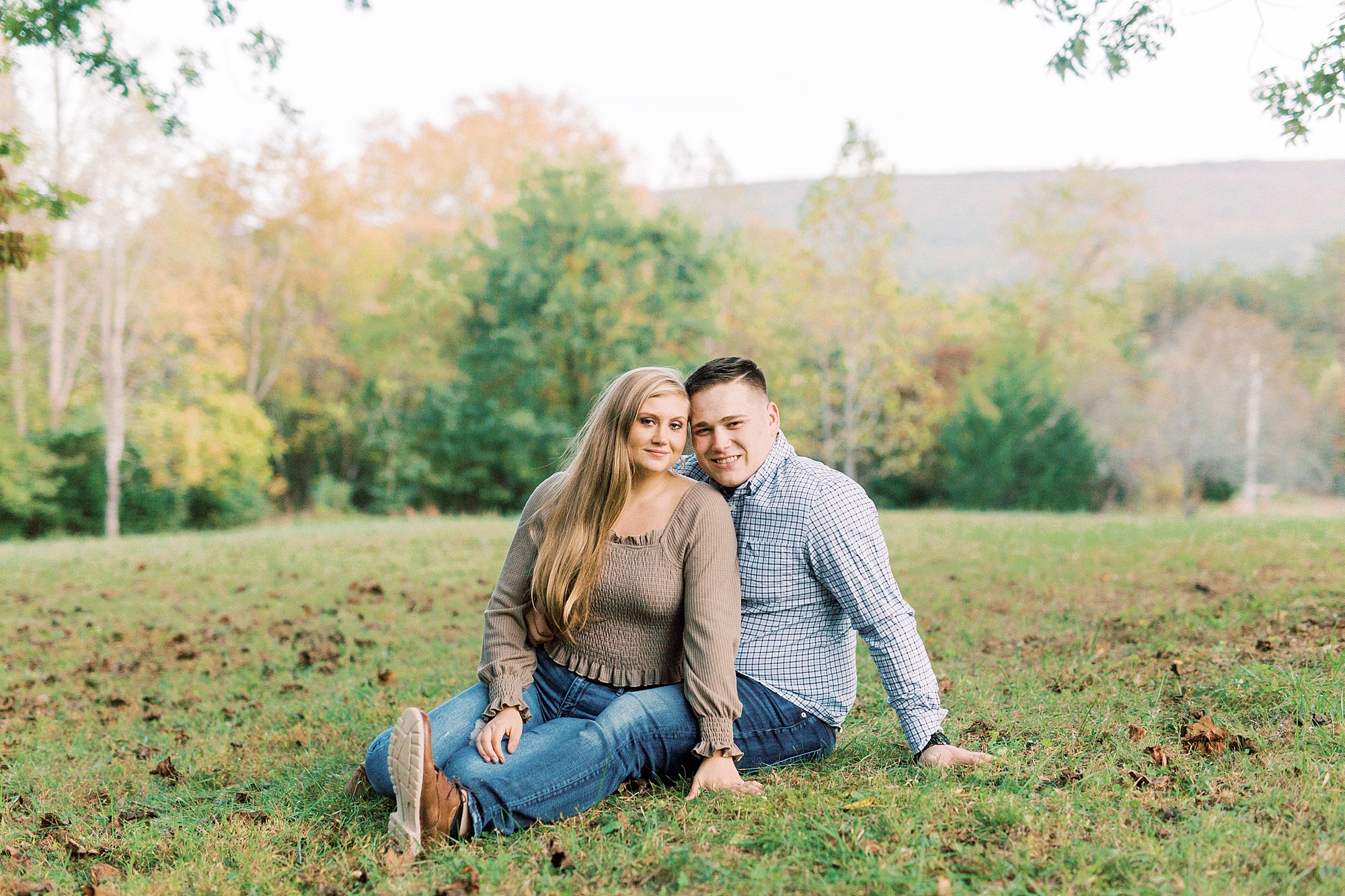 bride and groom sit in leaves during fall engagement session