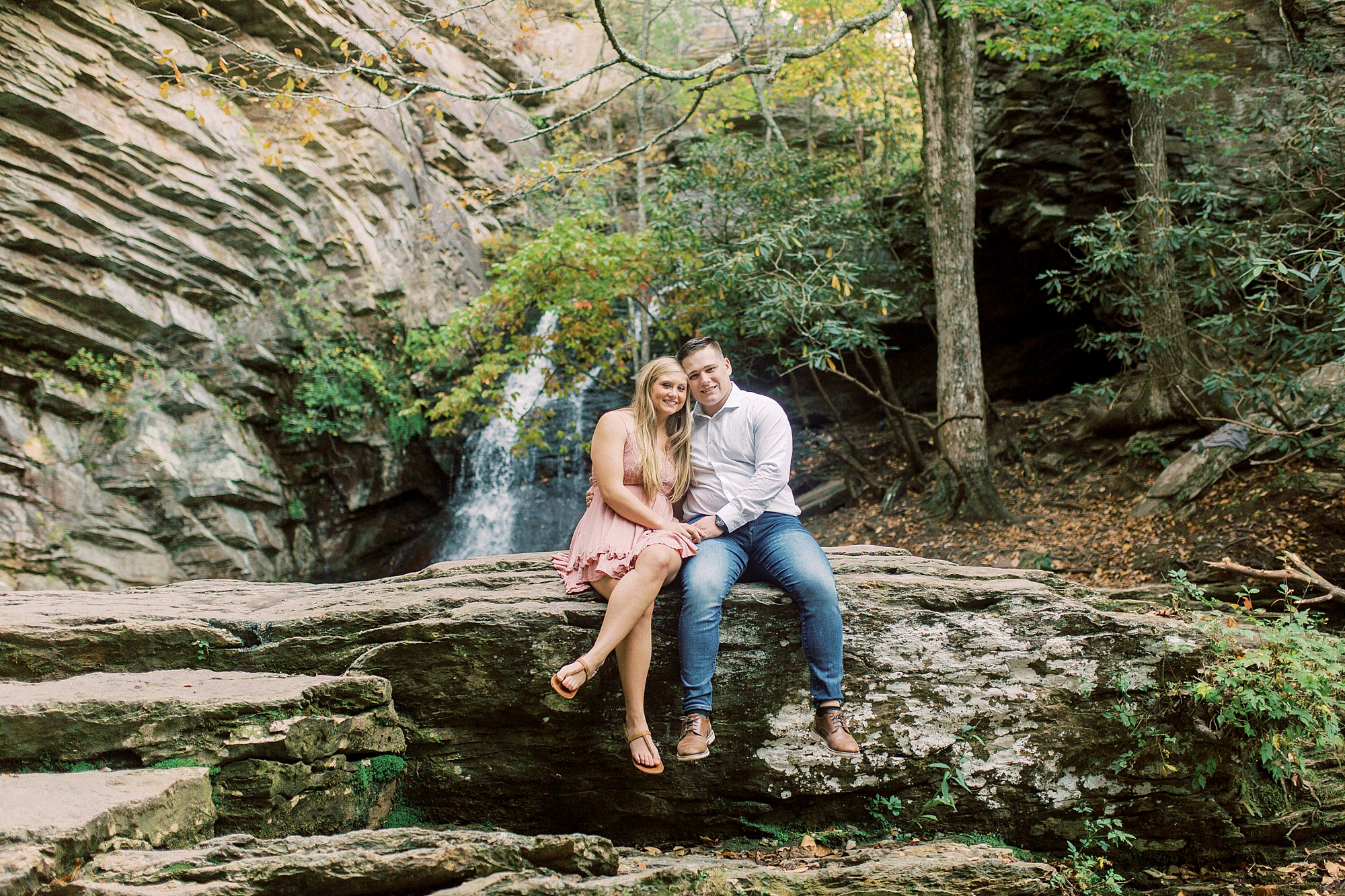 bride and groom sit on rock formation near waterfall