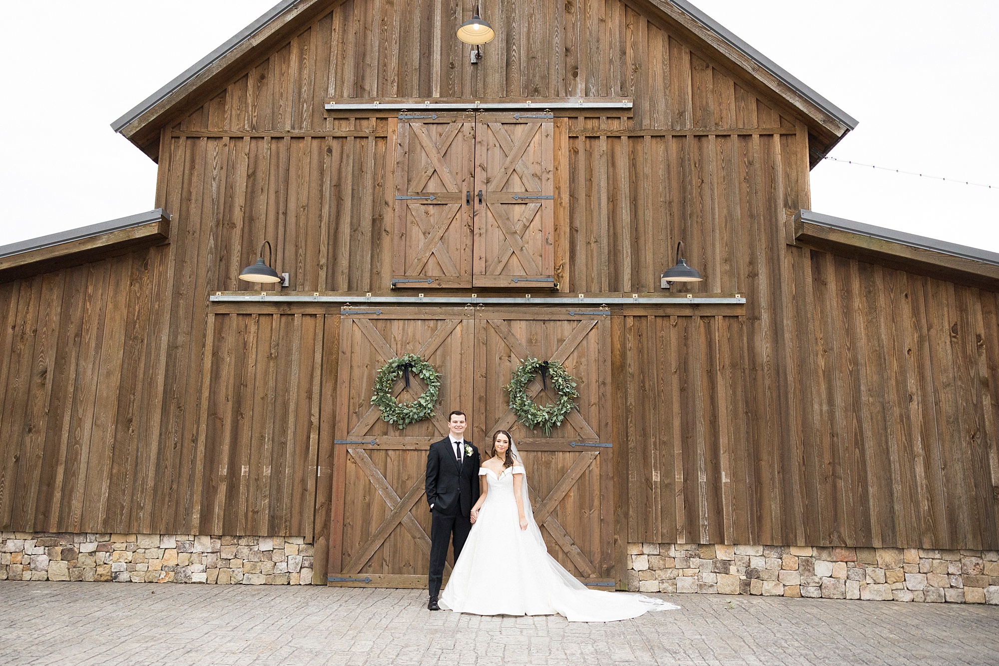 bride and groom stand by wooden doors of barn in Concord NC